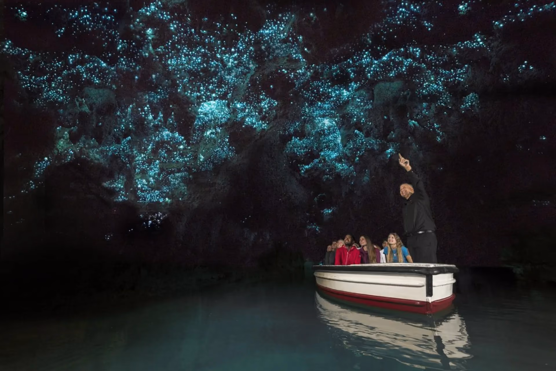 Boat full of visitors under glowing worms, New Zealand cave