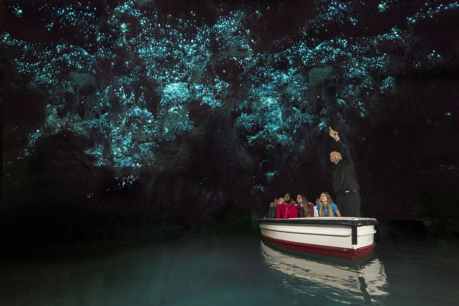 Boat full of visitors under glowing worms, New Zealand cave