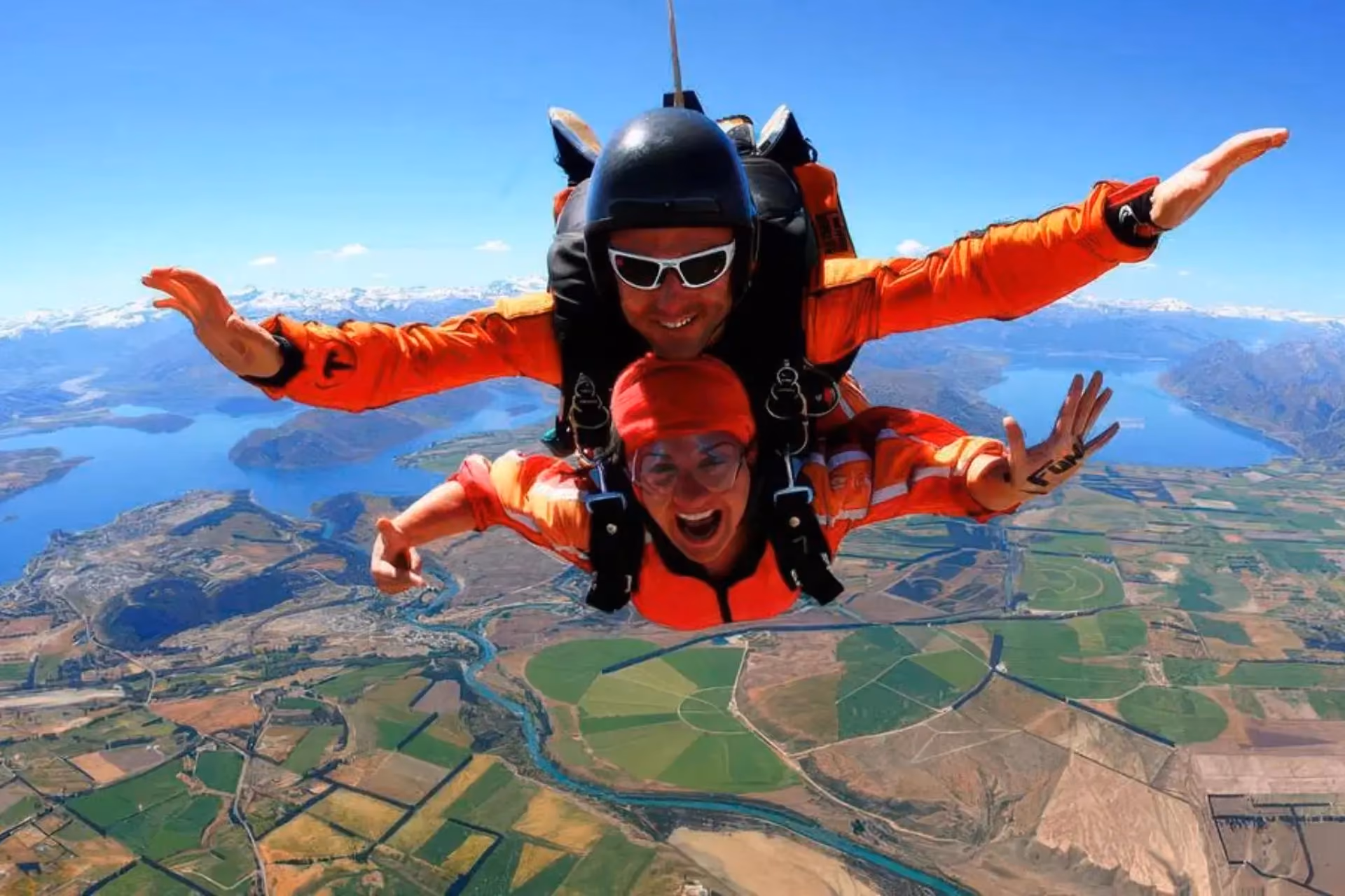 Two skydivers in red jump suits falling over New Zealand landscape