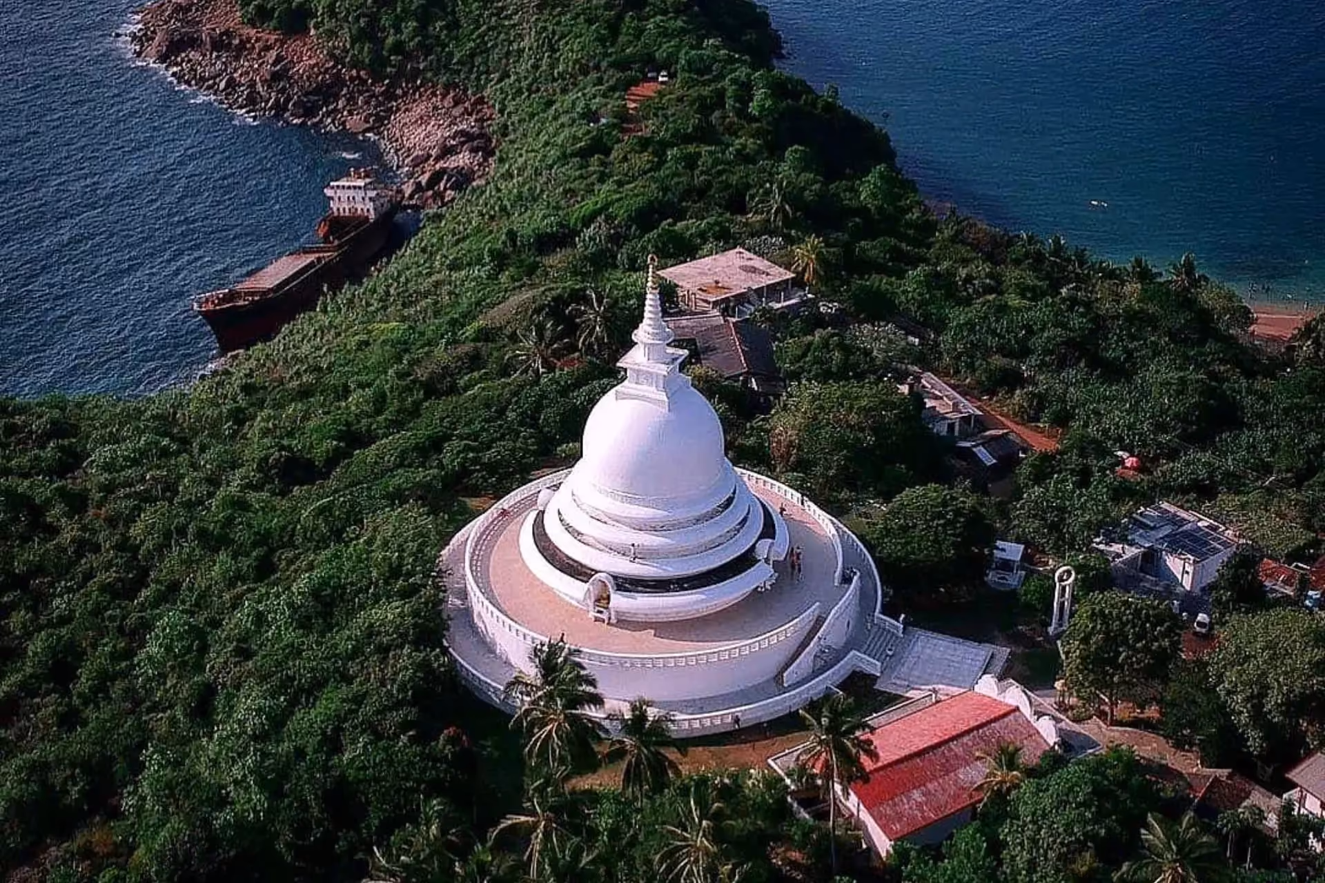 White dome pagoda surrounded by green trees and ocean