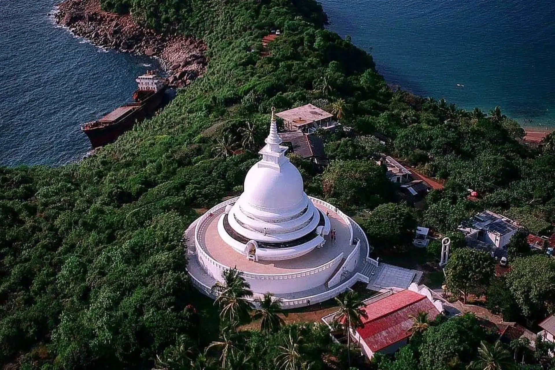 White dome pagoda surrounded by green trees and ocean