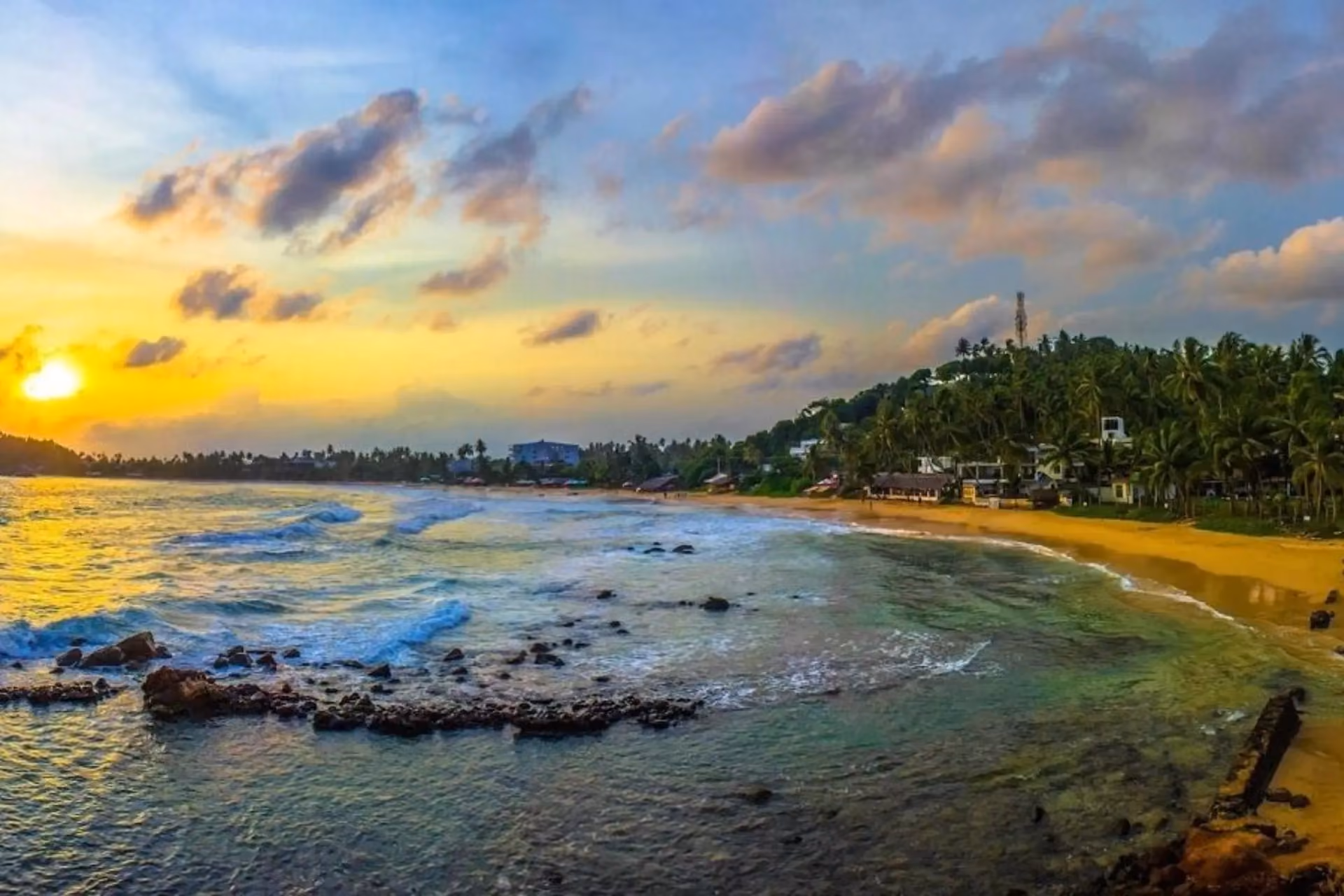 Sunset over Mirissa Beach with waves and palm trees