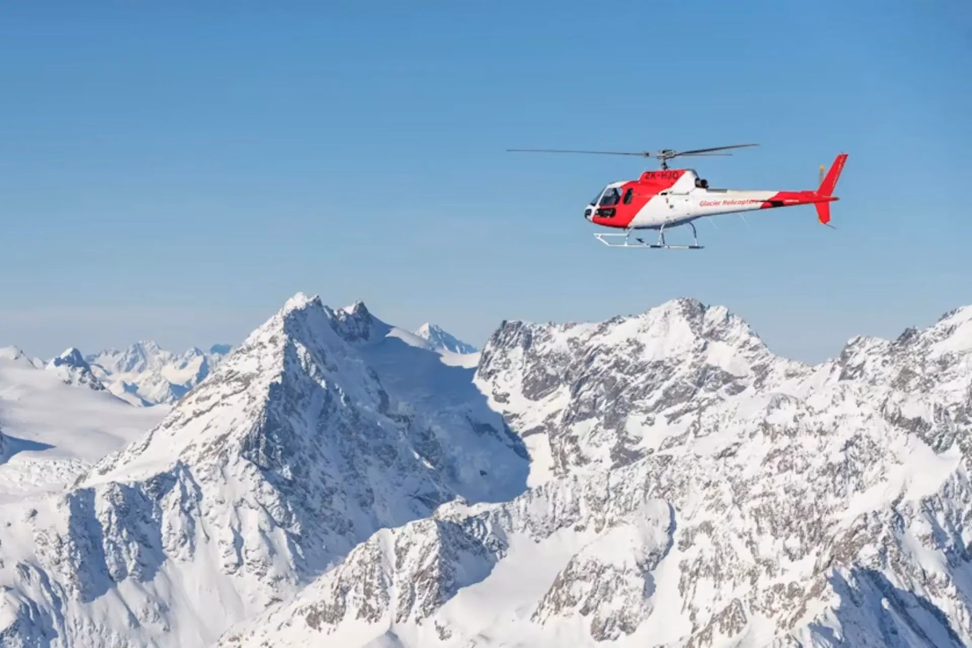 Red and white helicopter flying over snowy Mount Cook peaks