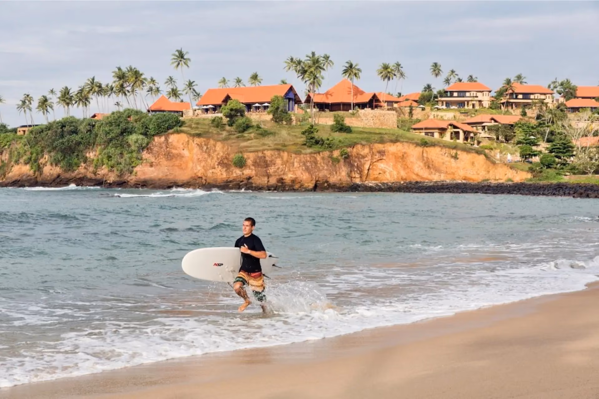 Surfer carrying board into ocean in Sri Lanka