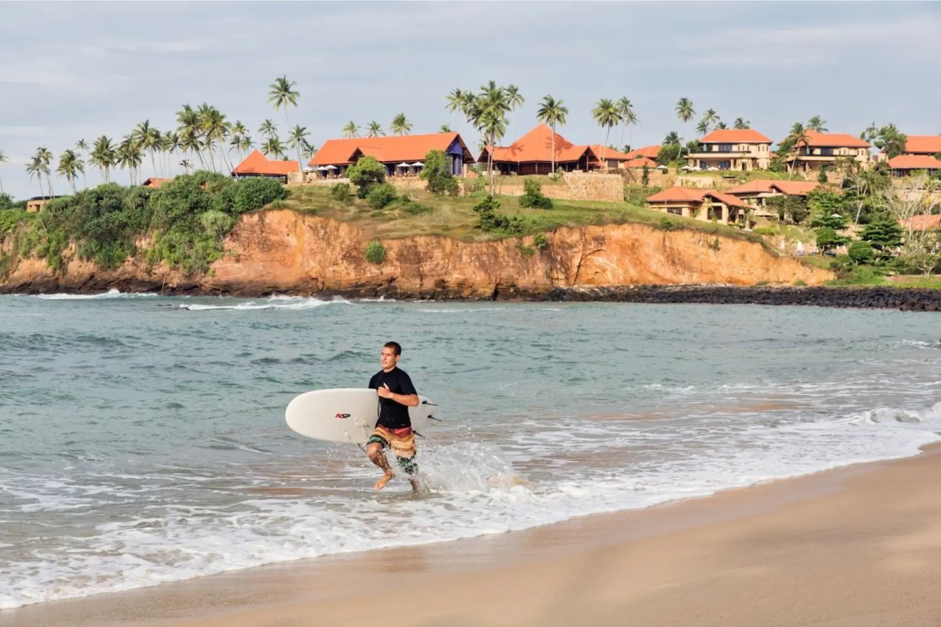 Surfer carrying board into ocean in Sri Lanka