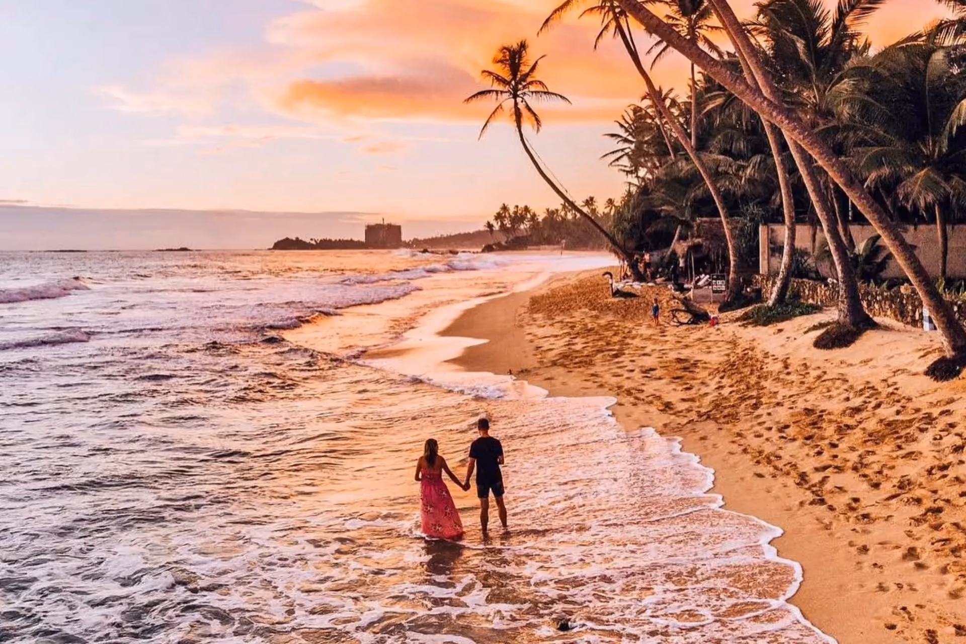 Couple wading in water at Unawatanu Beach at sunset