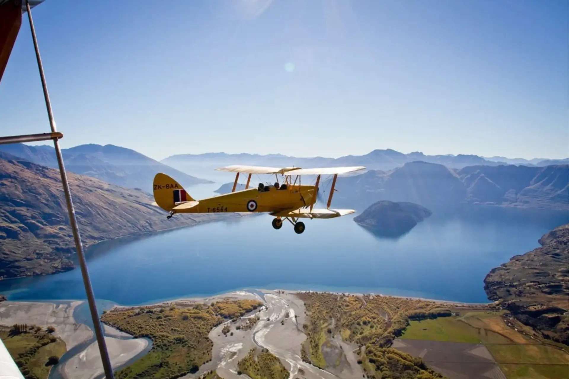 Yellow biplane flying over Lake Wanaka, New Zealand
