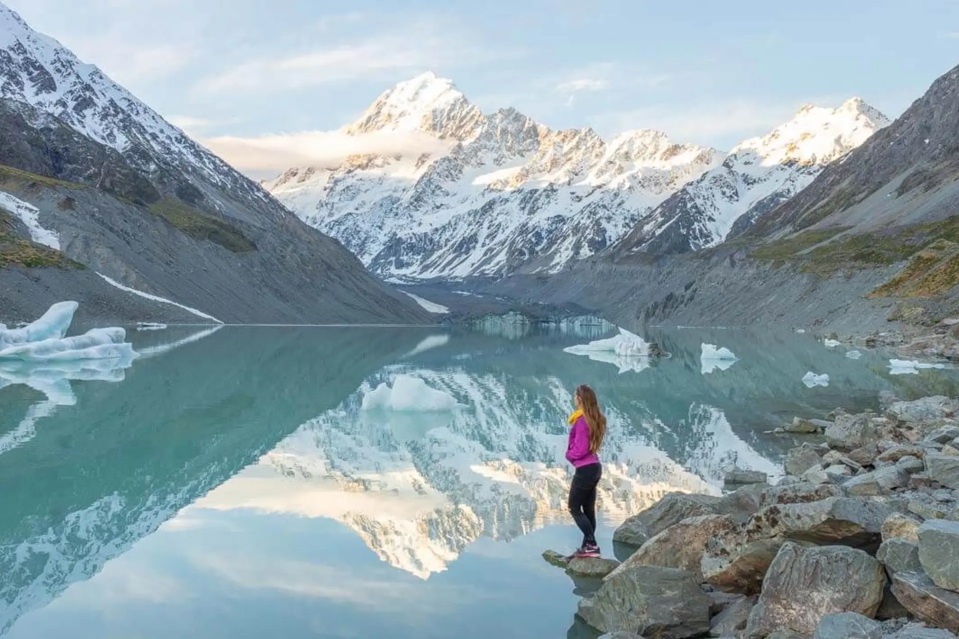 Woman standing on rocks by glacial lake, Hooker Valley Track