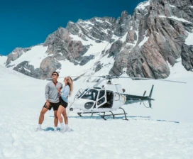 Two people standing on snow next to helicopter at Mount Cook