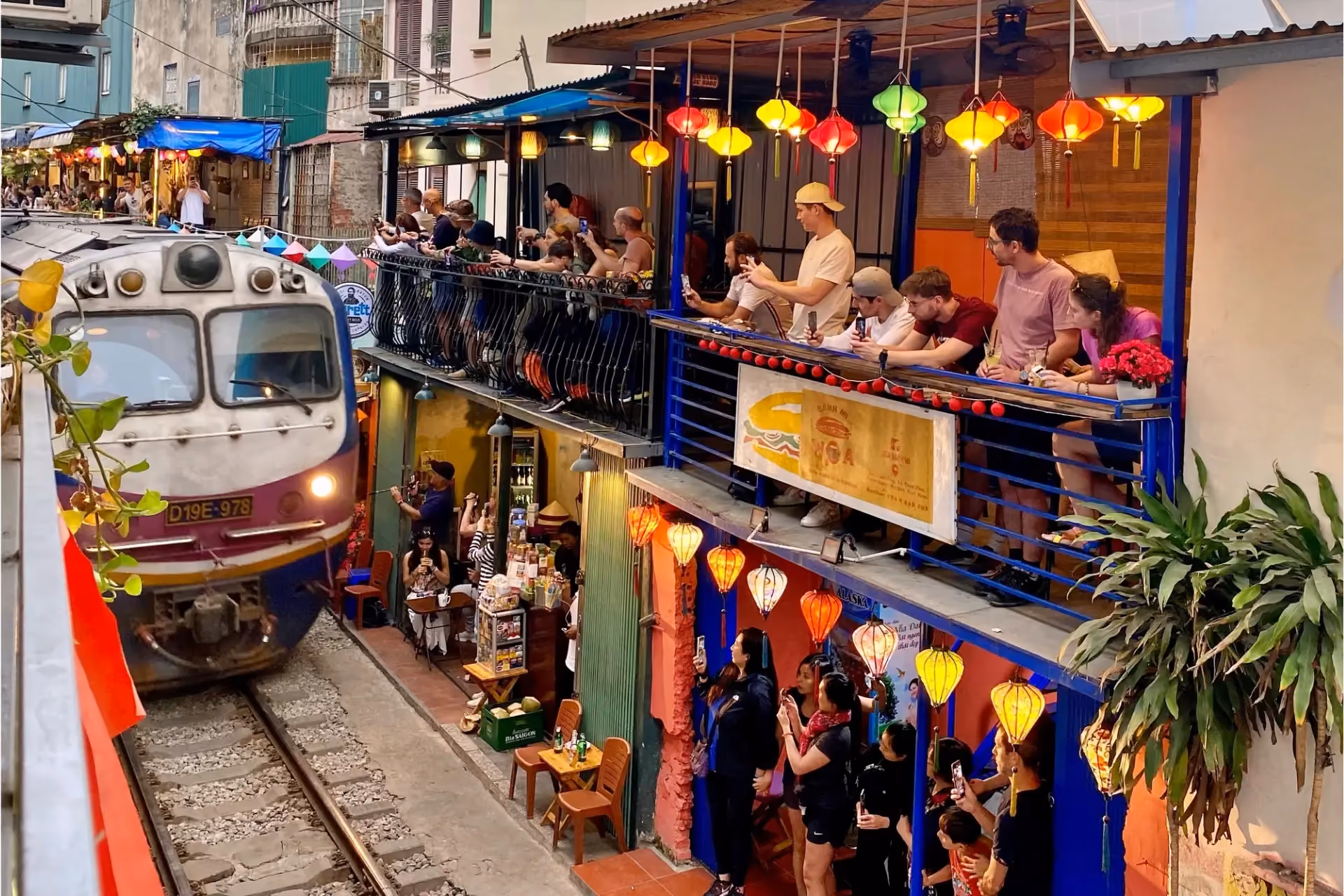 Train passing through Hanoi Train Street with restaurants and lanterns