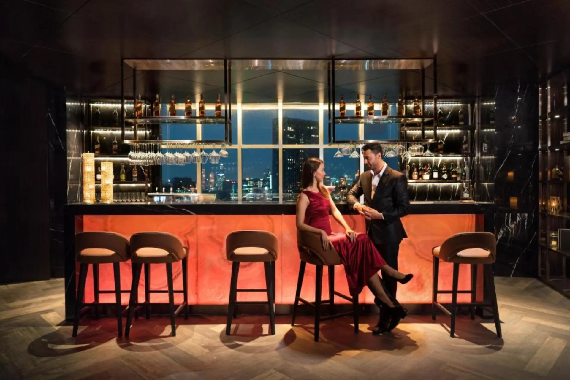 Couple chatting at bar with city lights behind them