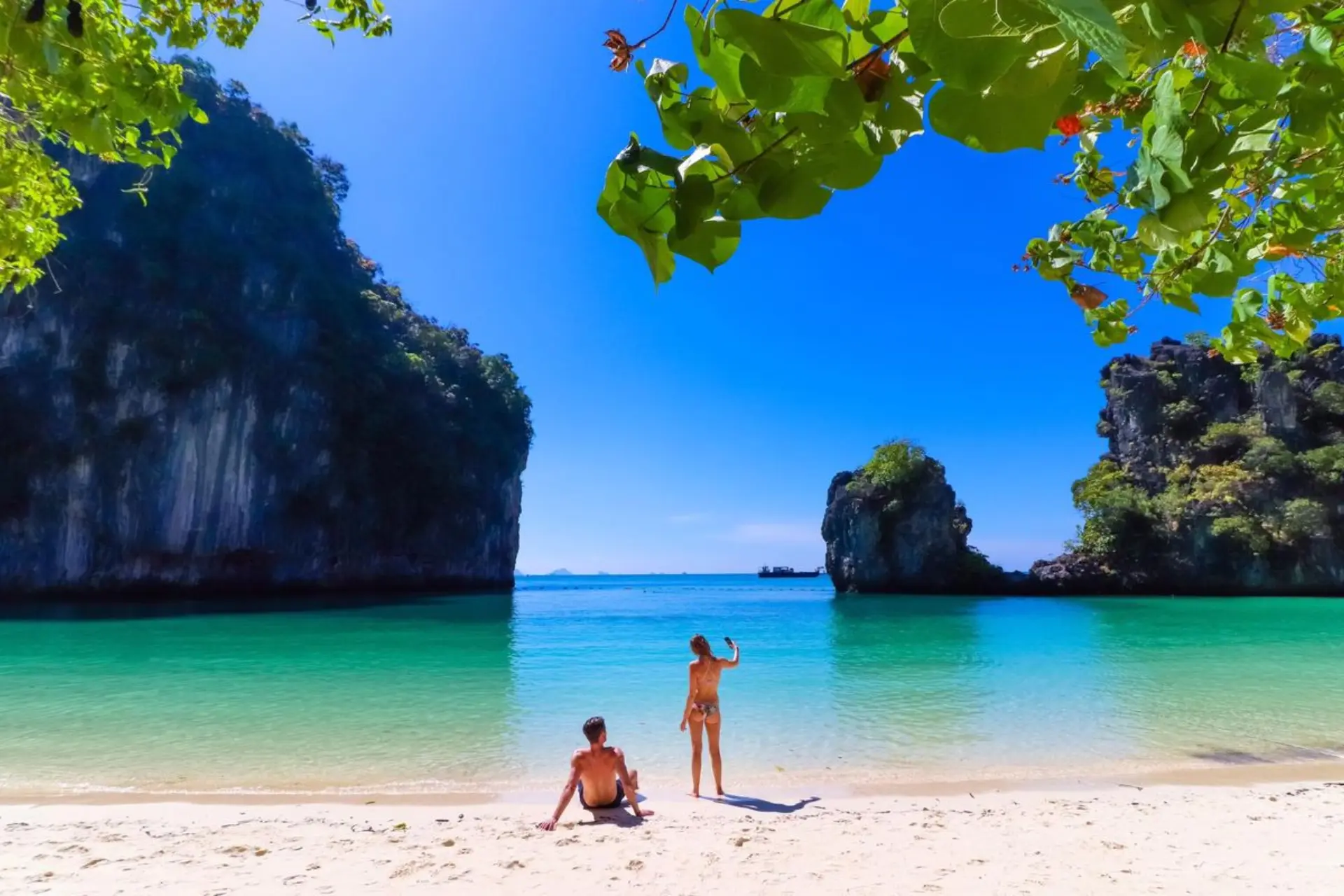Two people on beach with tall rocks and clear blue water, Thailand