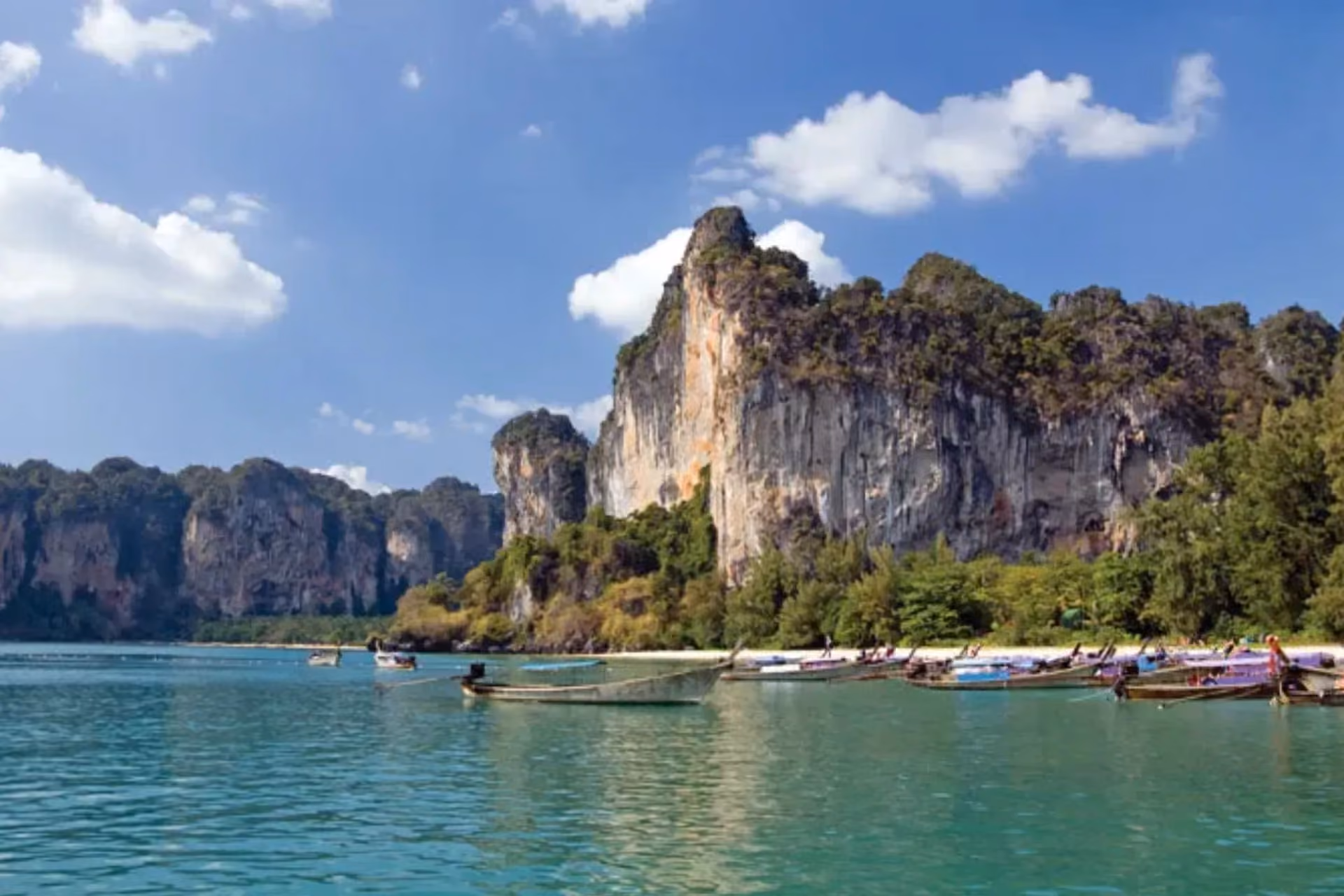 Tall cliff and boats on clear water in Krabi
