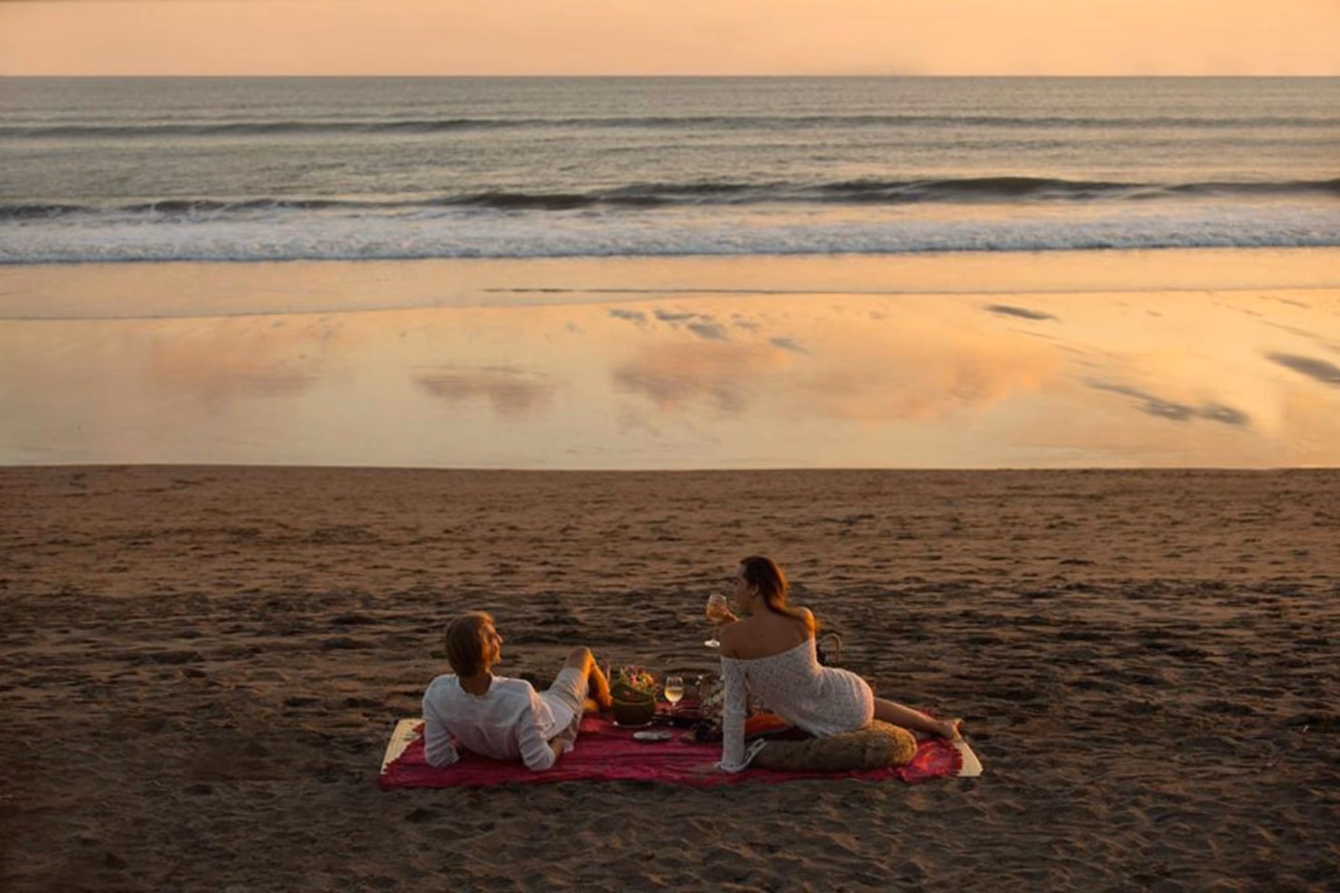 Two women sitting on red blanket at beach sunset