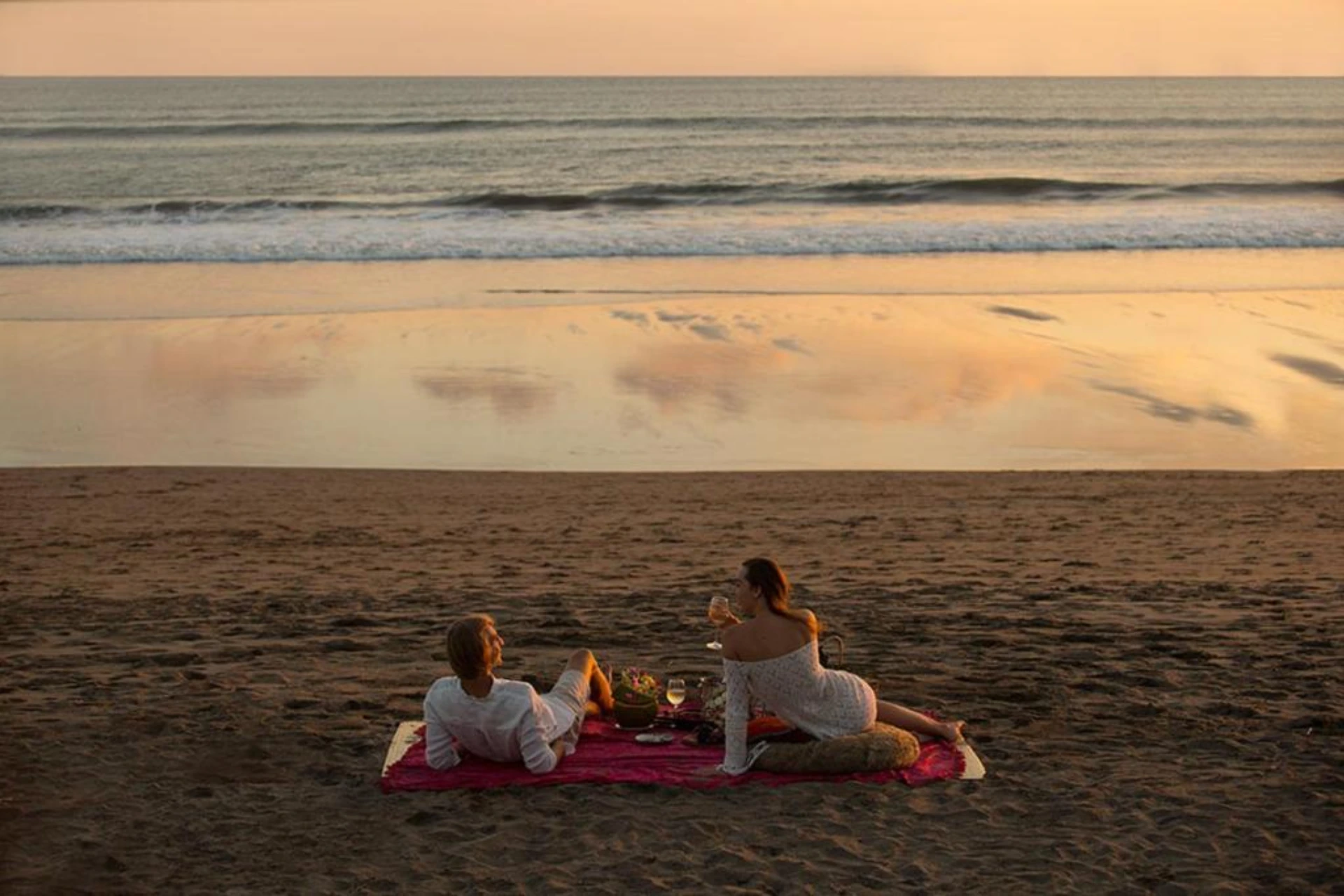Two women sitting on red blanket at beach sunset