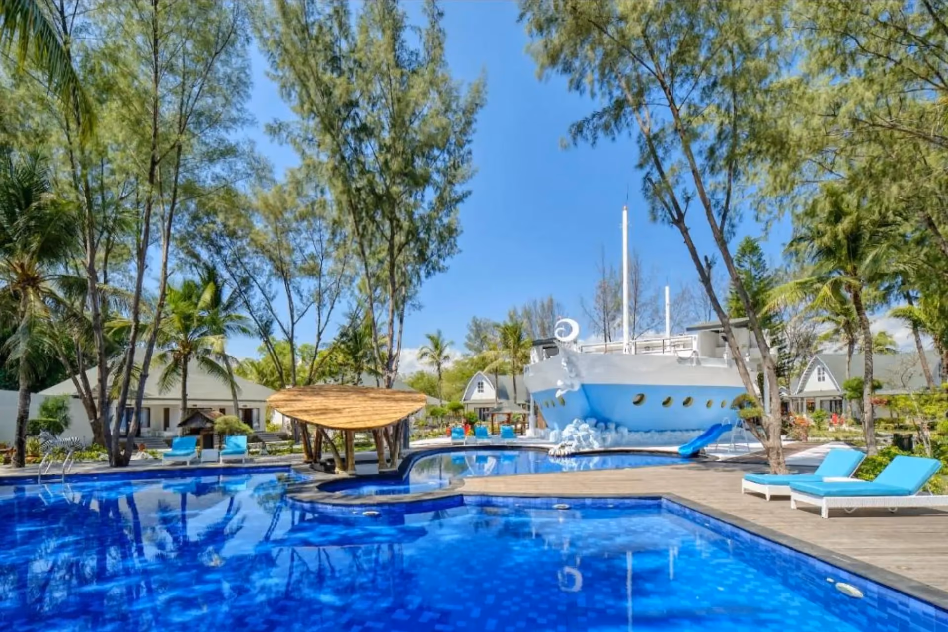 Jambuluwuk resort pool with blue loungers and ship-shaped building