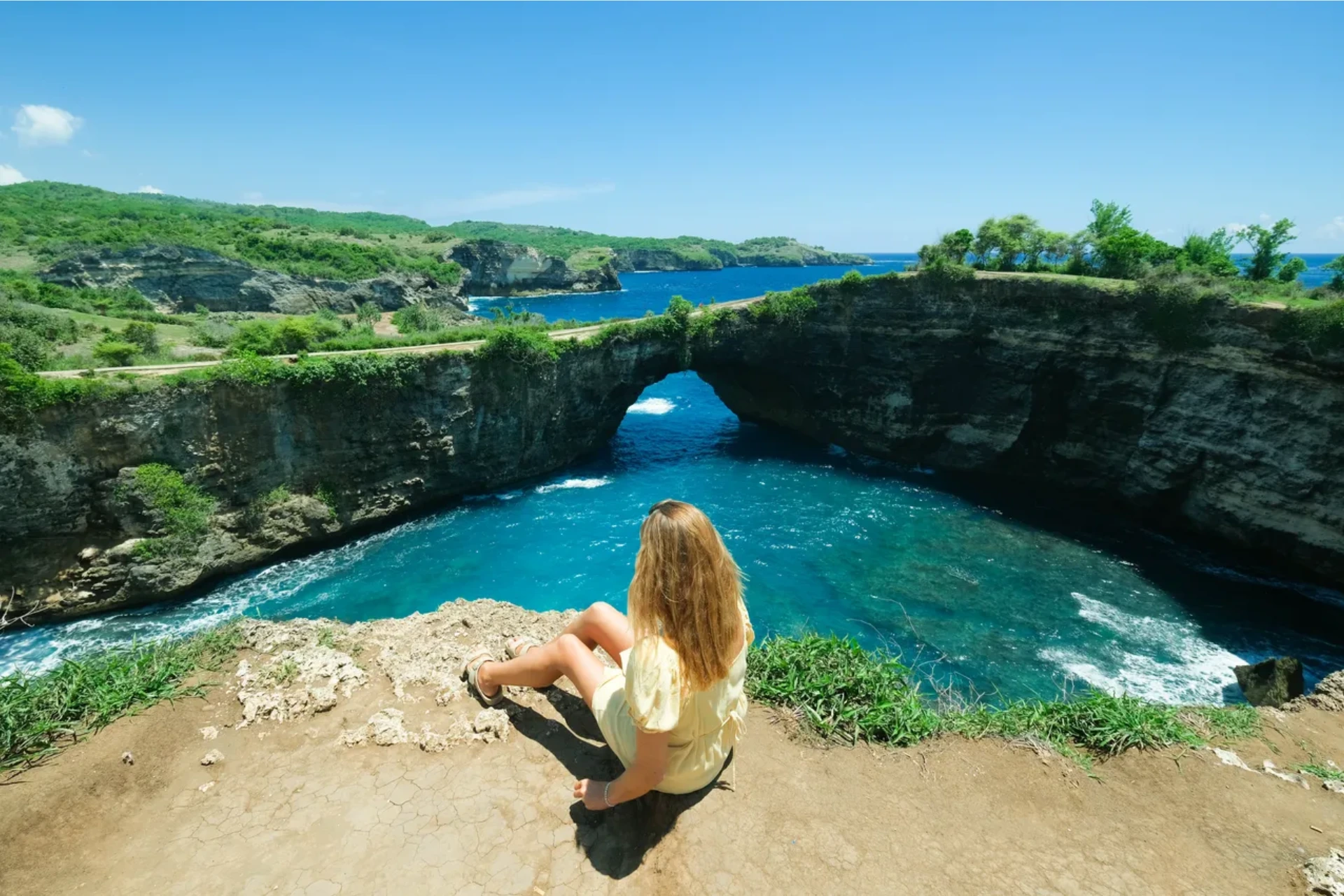 Woman sitting on cliff overlooking Broken Beach's blue water