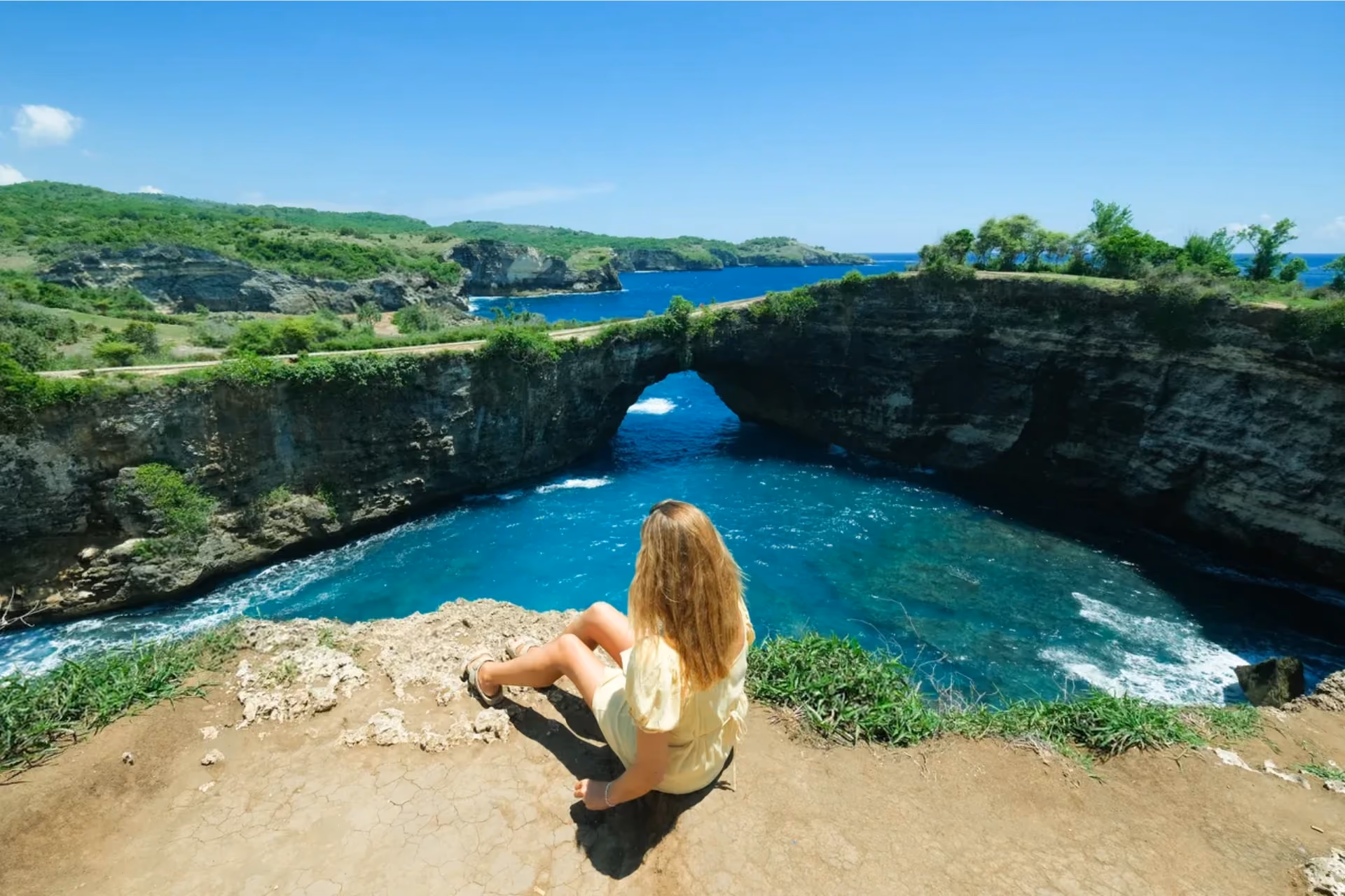 Woman sitting on cliff overlooking Broken Beach's blue water