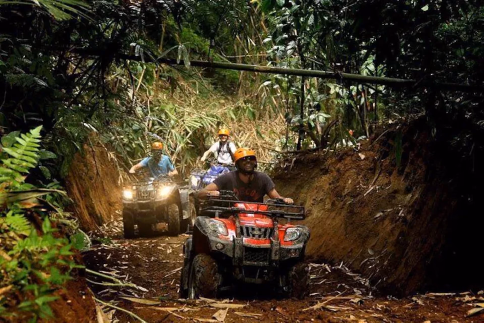 Three people riding red ATVs on muddy jungle trail in Bali