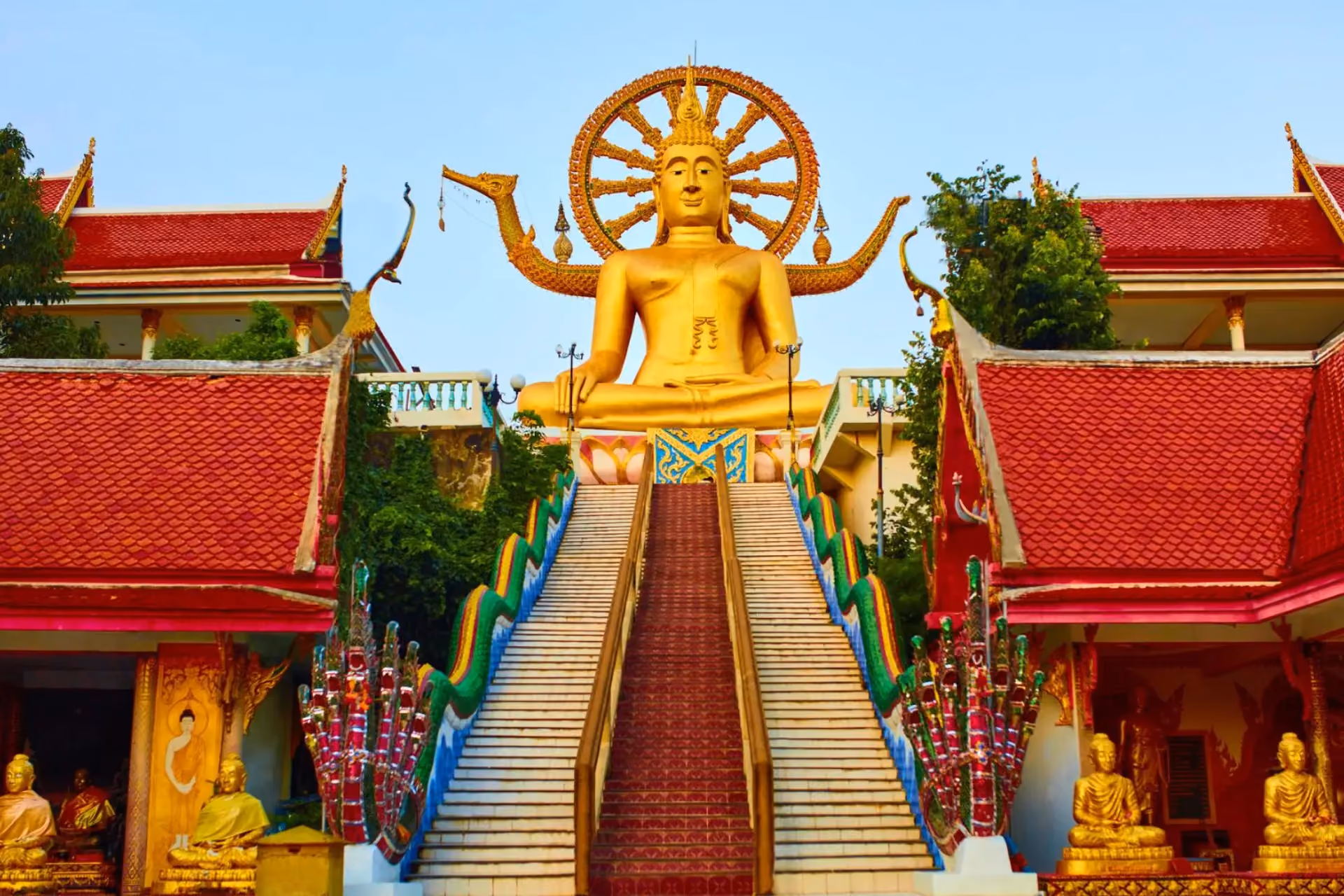 Giant gold Buddha statue at Koh Samui temple with red roofs