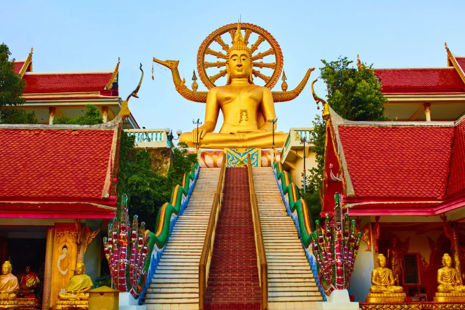 Giant gold Buddha statue at Koh Samui temple with red roofs