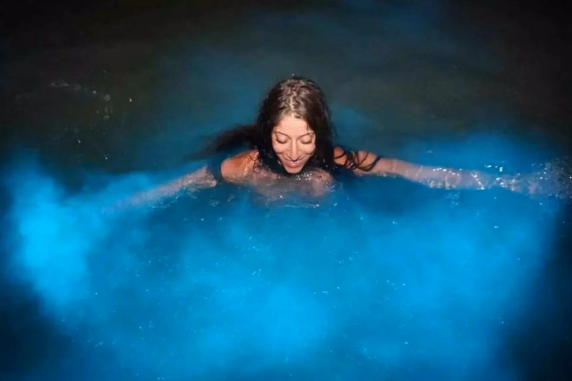 Woman snorkeling in glowing blue water at night