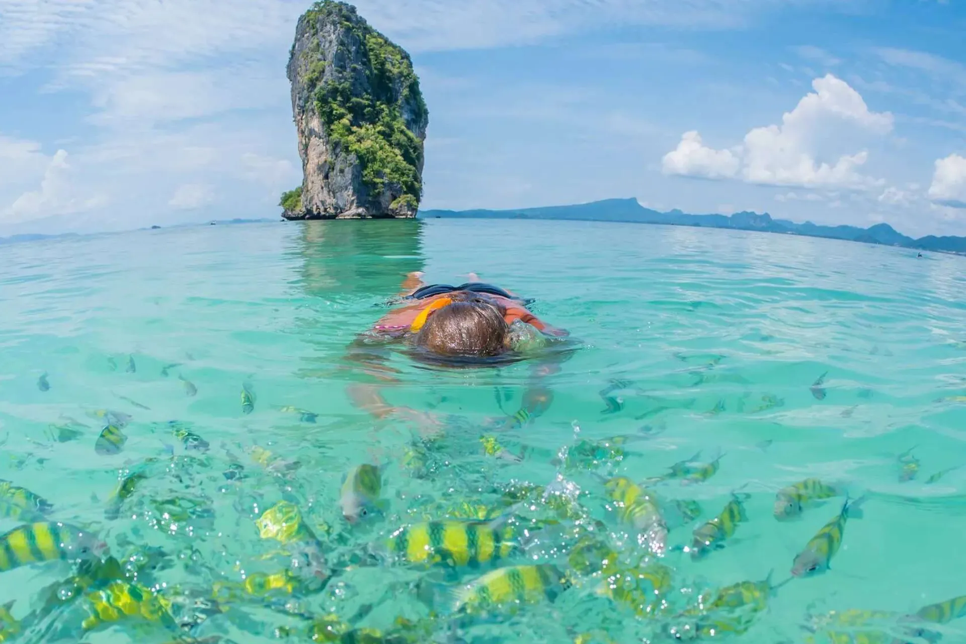 Person snorkeling in clear water near tall rock, Krabi Thailand