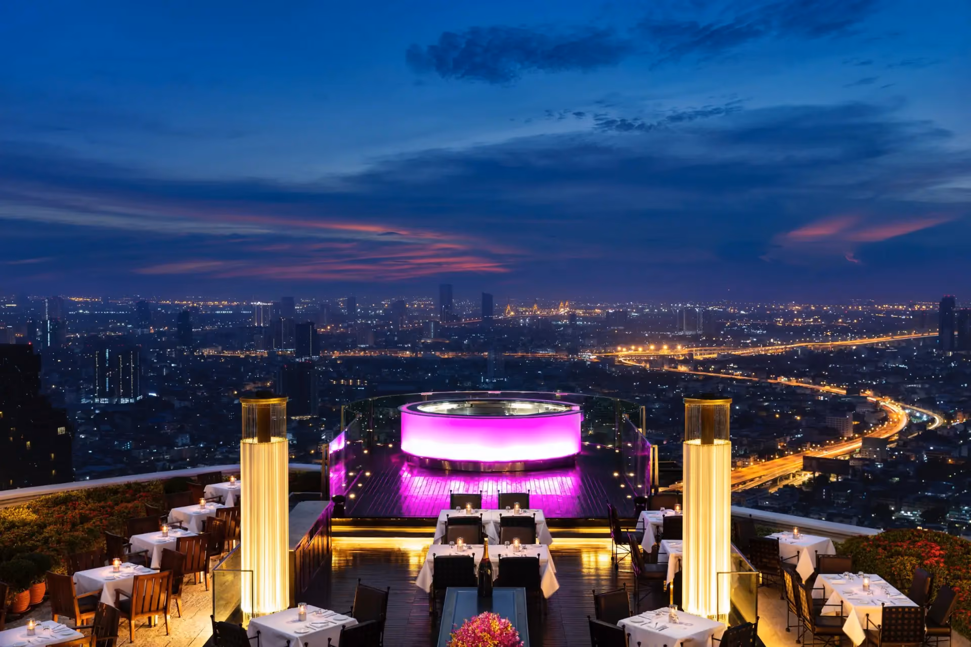 Rooftop restaurant with pink lights overlooking Thai city at night