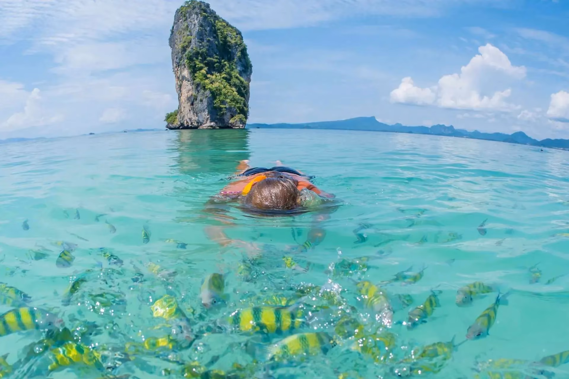 Person snorkeling in clear water near tall rock, Krabi Thailand