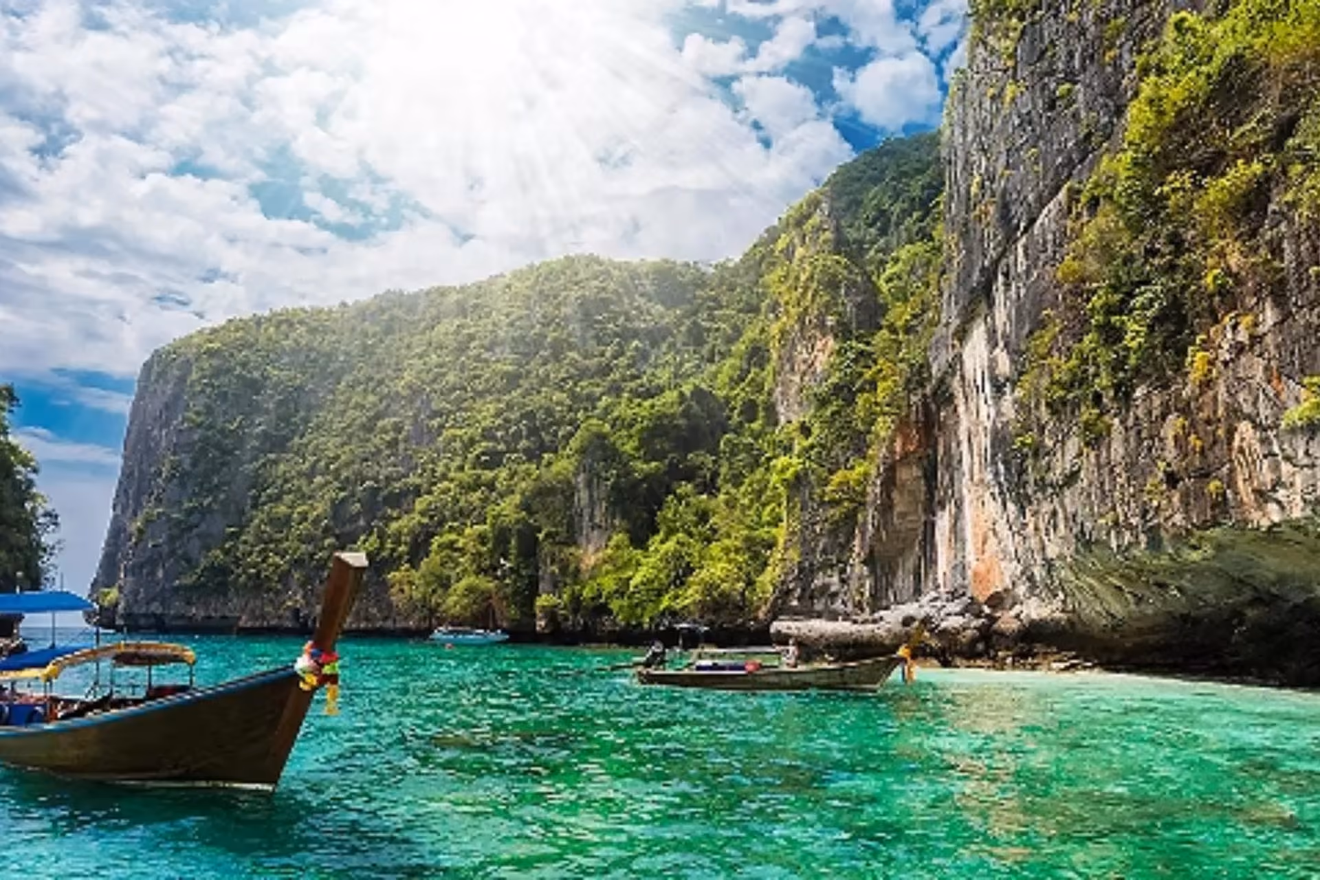 Wooden boats in clear green water at Phuket cliff bay