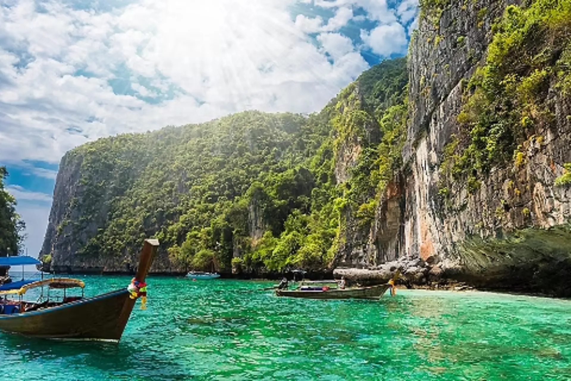 Wooden boats in clear green water at Phuket cliff bay