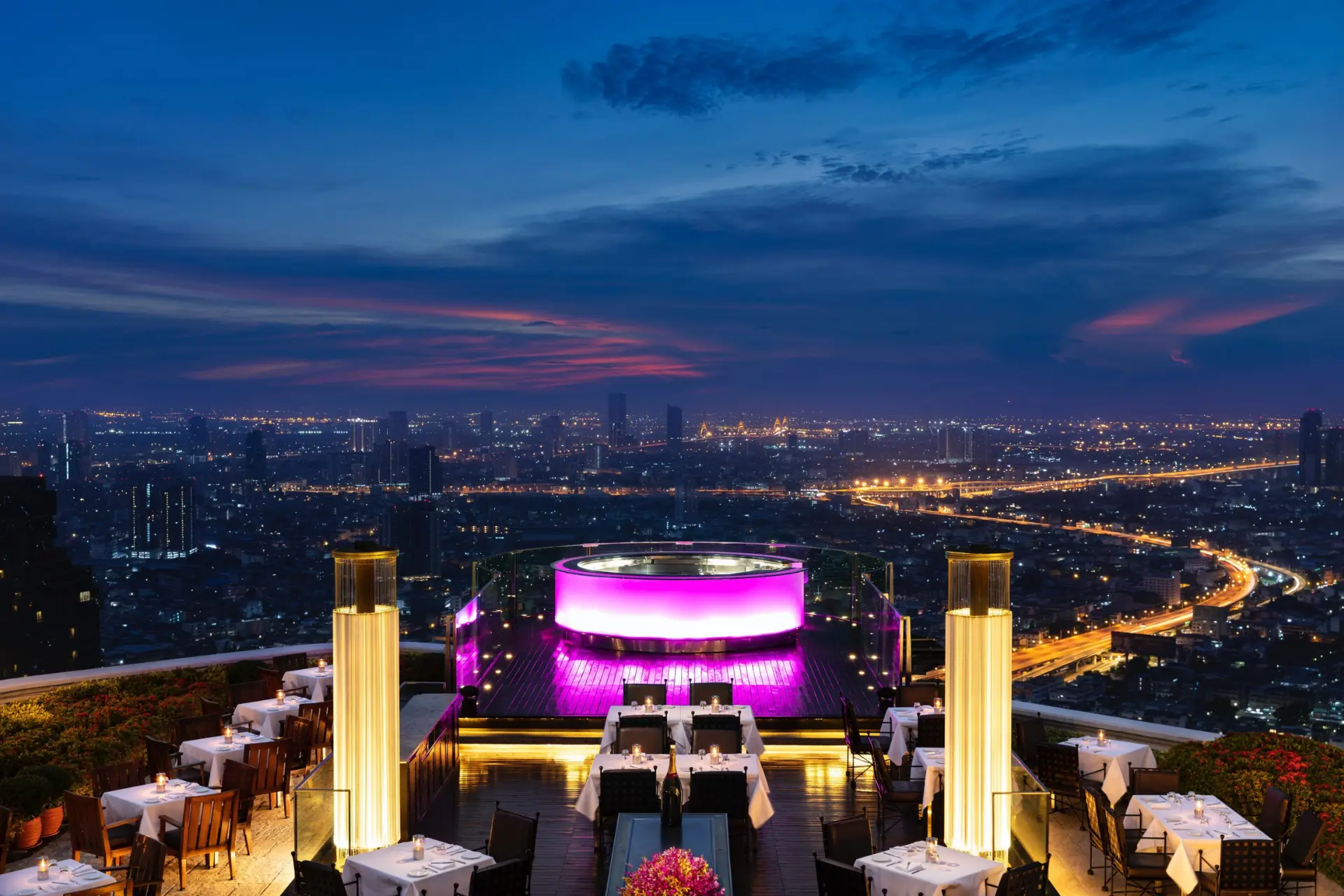Rooftop restaurant with pink lights overlooking Thai city at night
