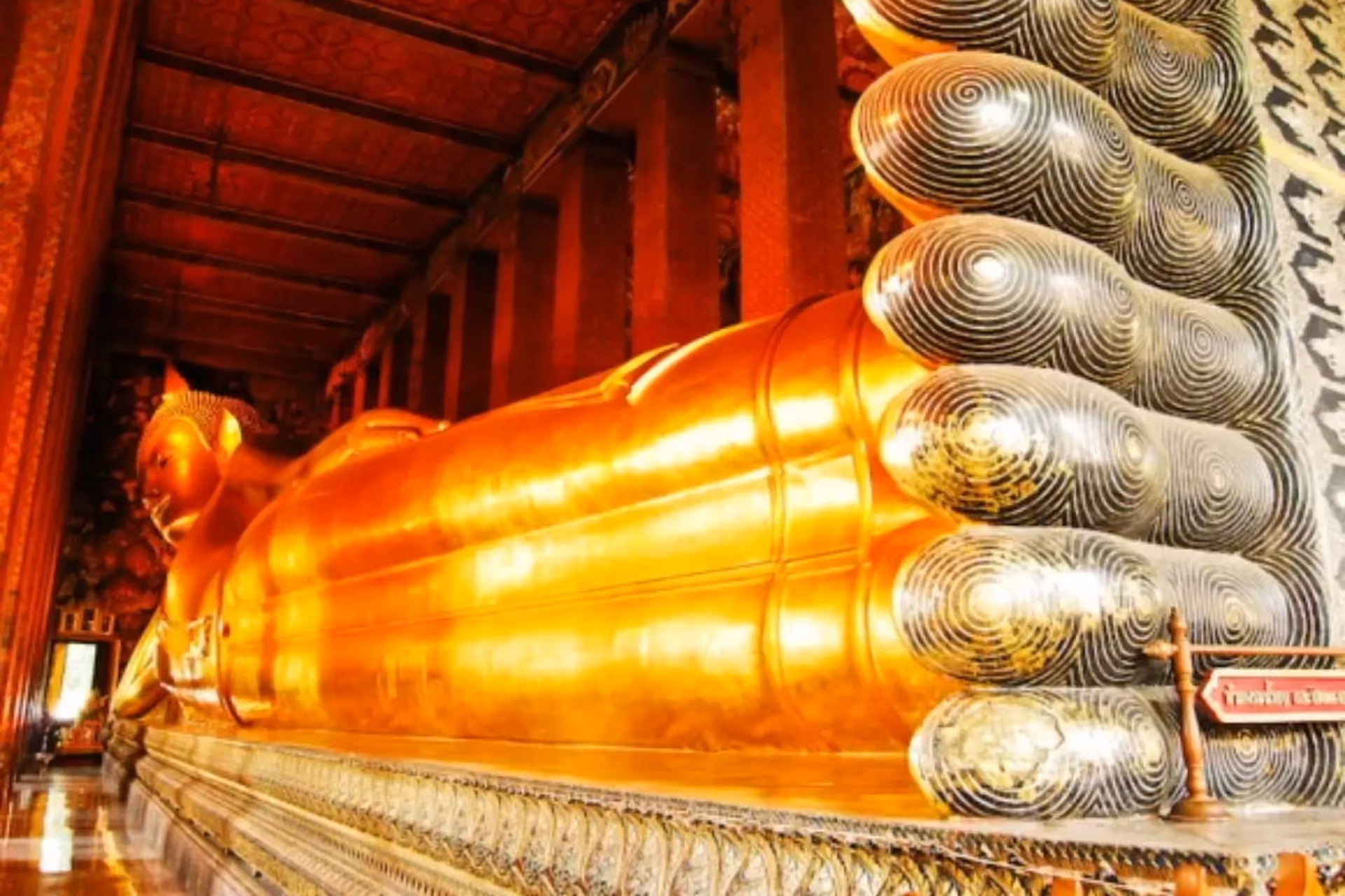 Gold reclining Buddha statue inside red temple hall