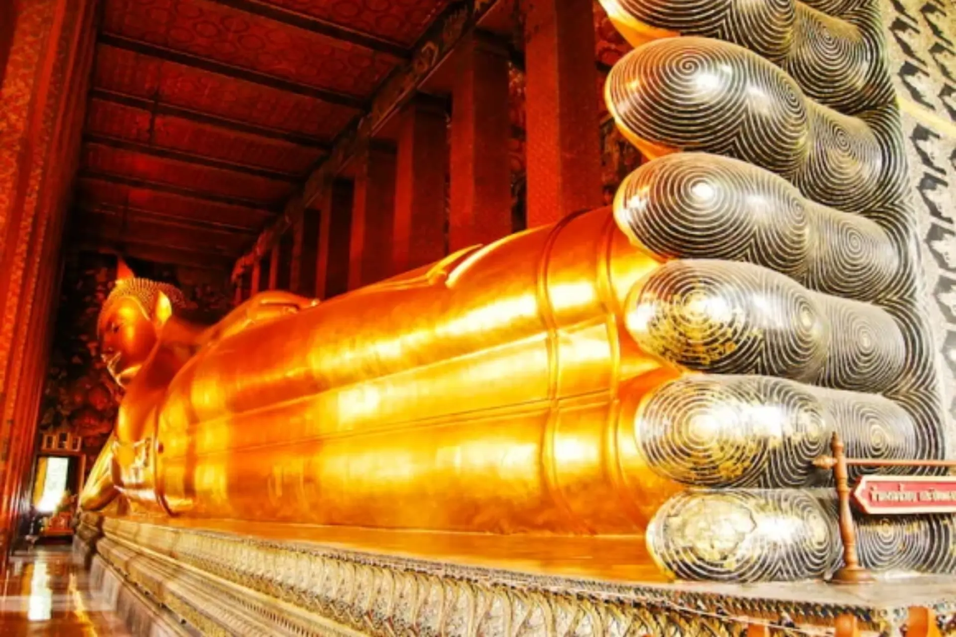 Gold reclining Buddha statue inside red temple hall