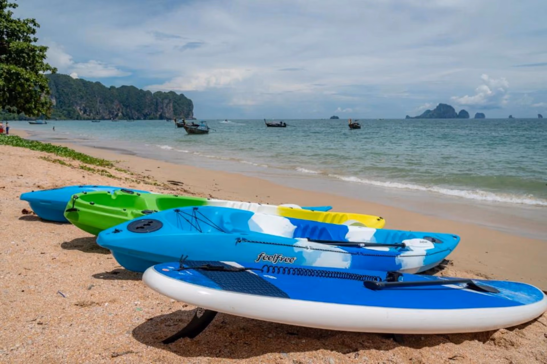 Colorful kayaks lined up on sandy beach with limestone islands.