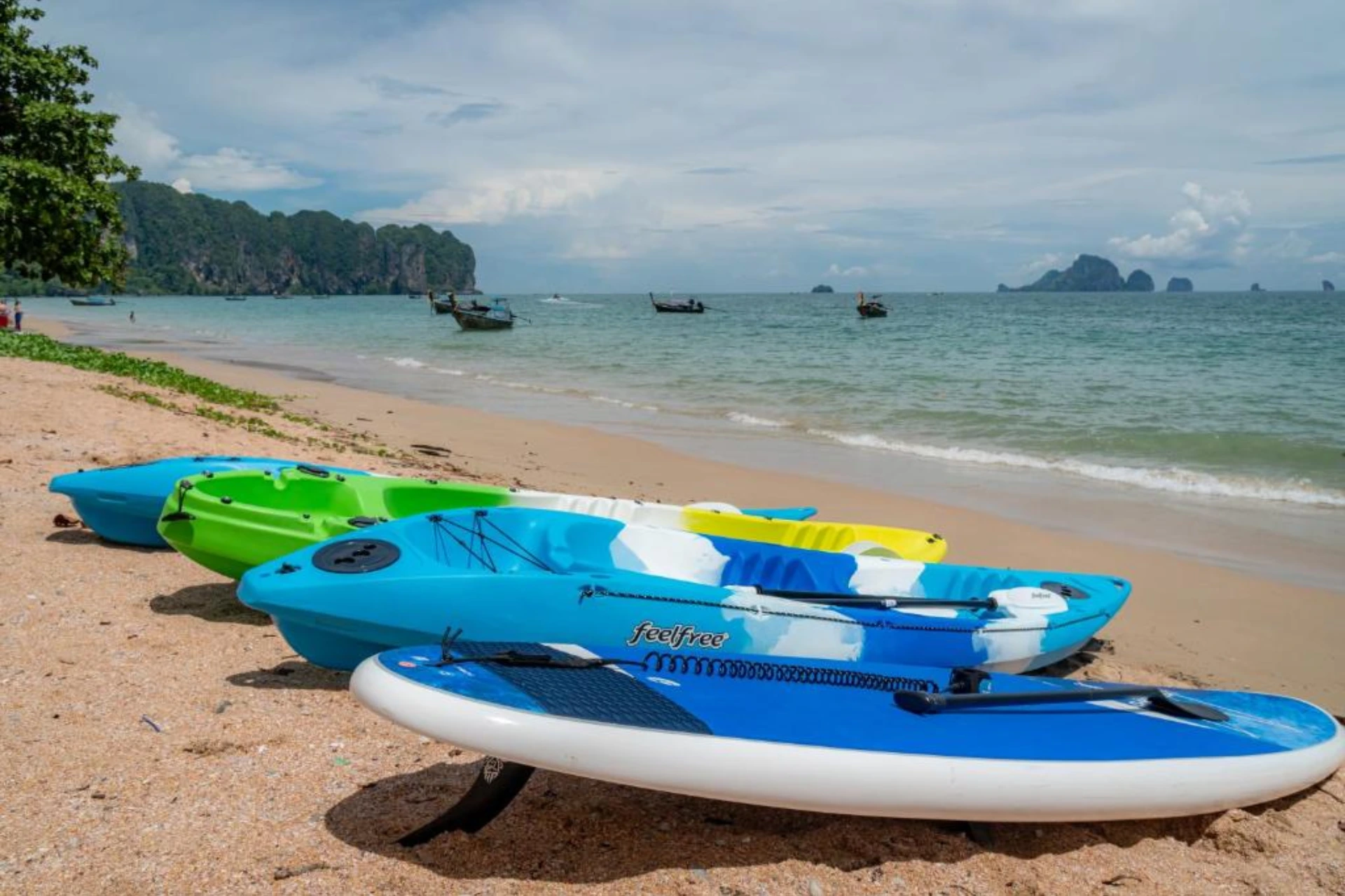 Colorful kayaks lined up on sandy beach with limestone islands.
