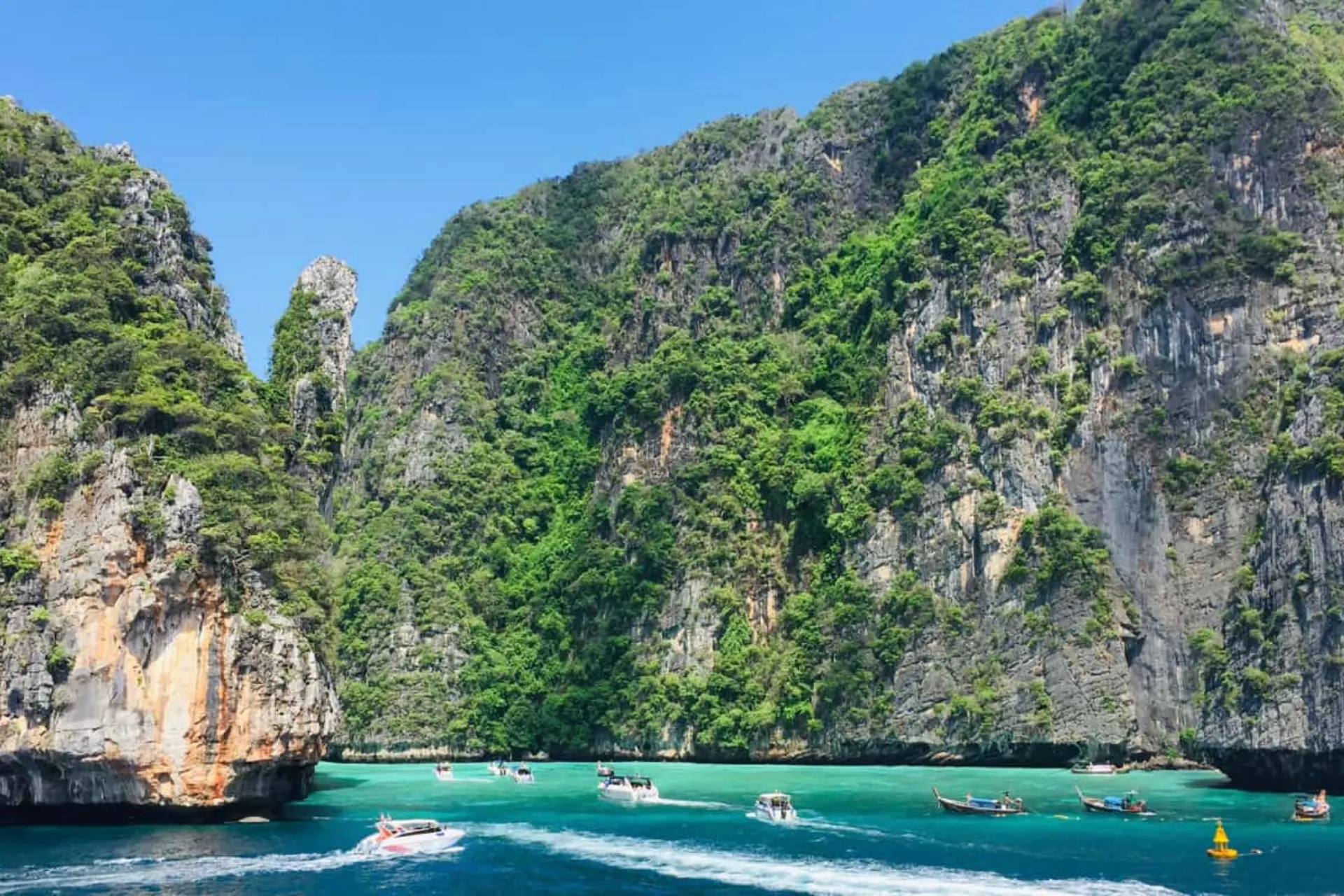 Boats on blue-green water between tall cliffs at Phi Phi