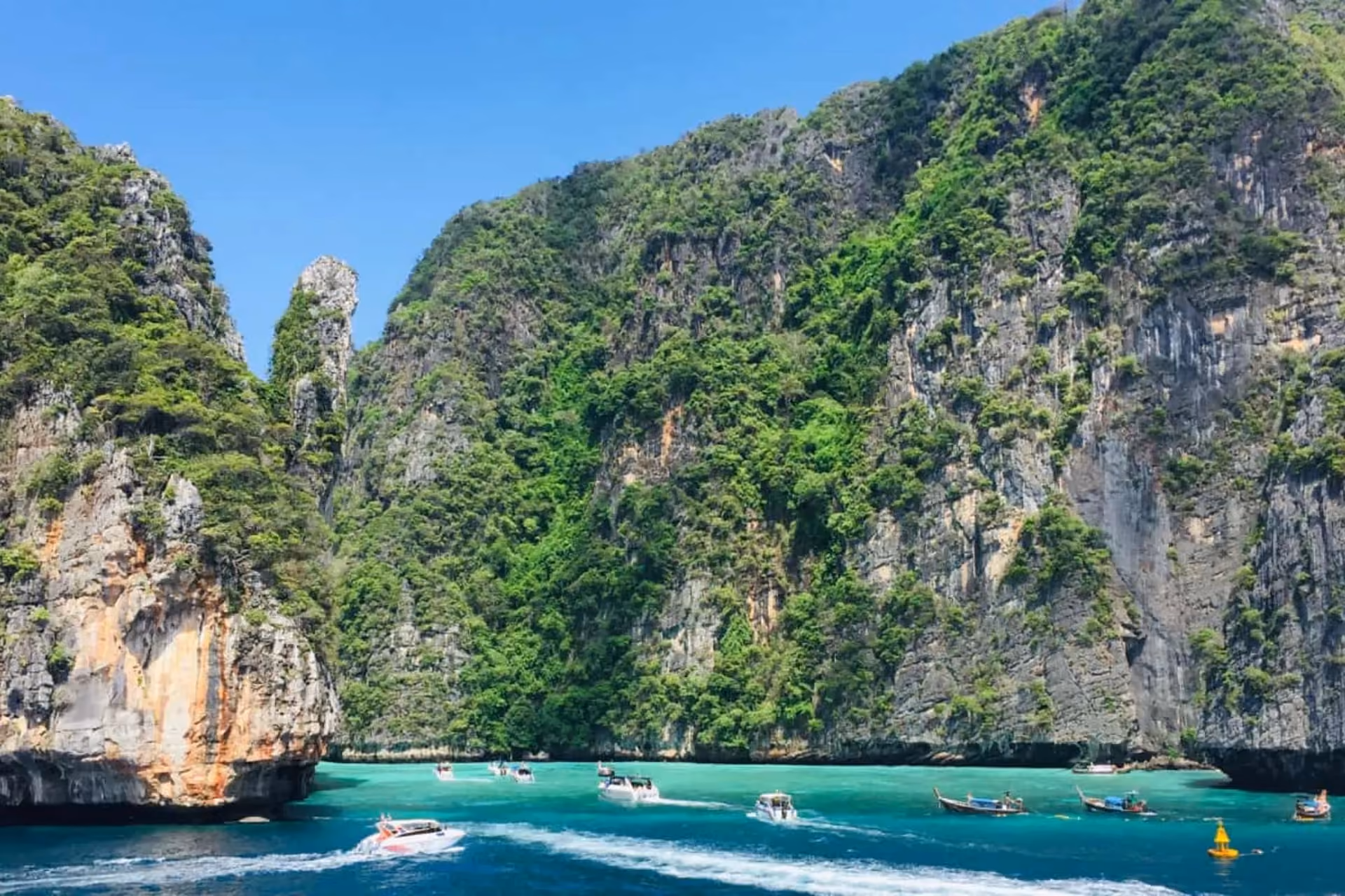 Boats on blue-green water between tall cliffs at Phi Phi