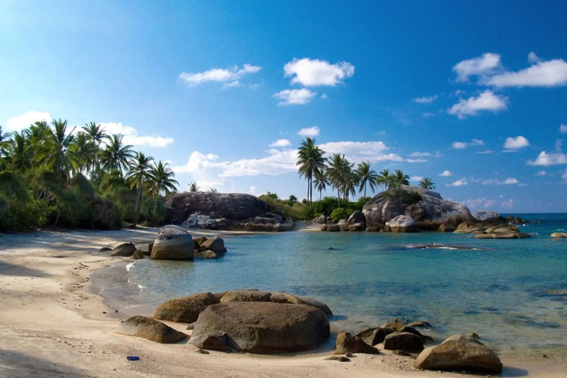 Bali beach with large rocks, palm trees, and blue water