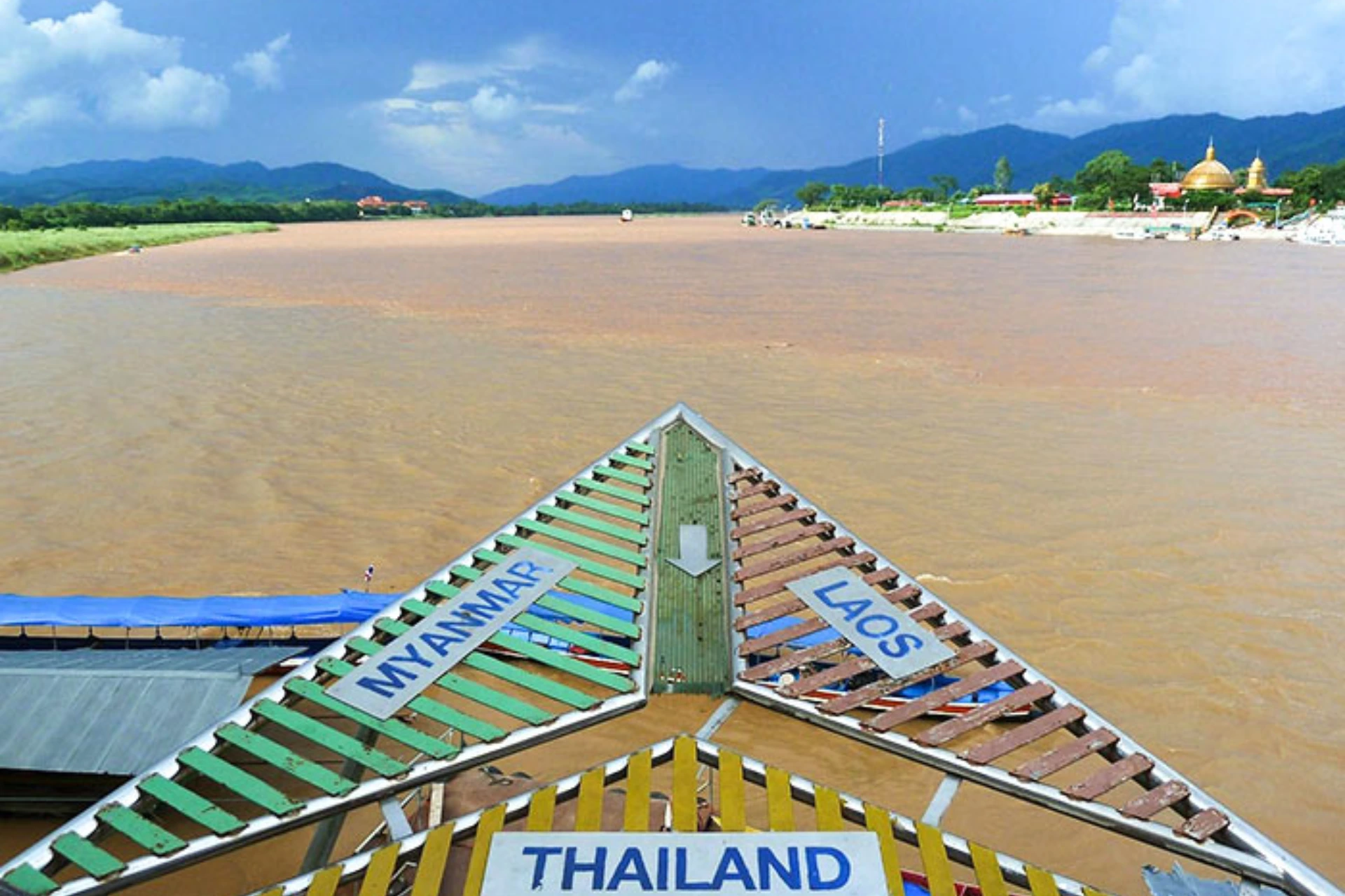 Boat bow with Thailand and Laos signs on river, mountains behind