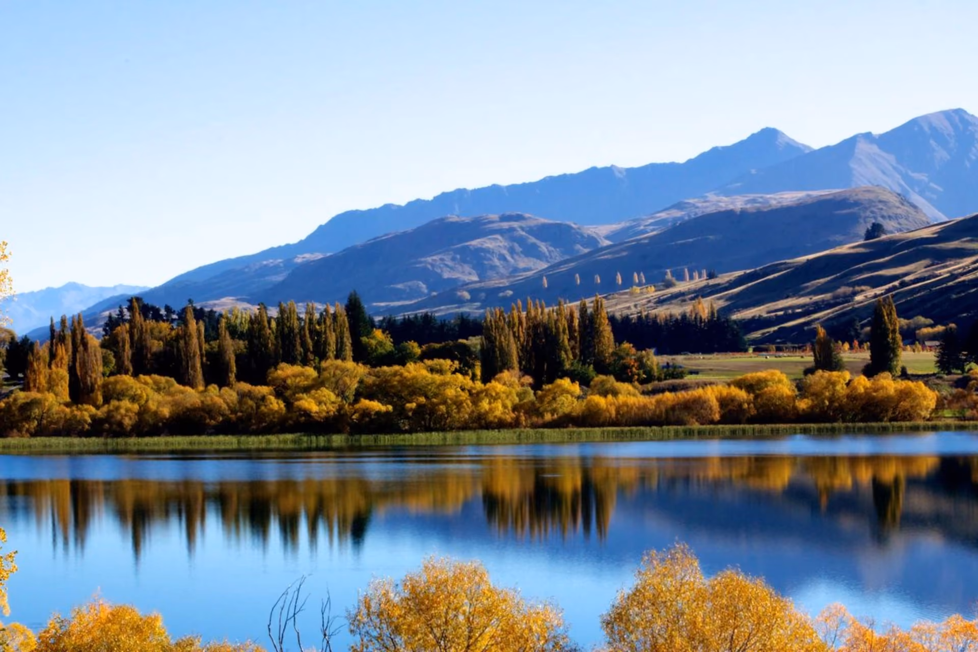 Lake Hayes New Zealand with mountains and autumn trees reflected
