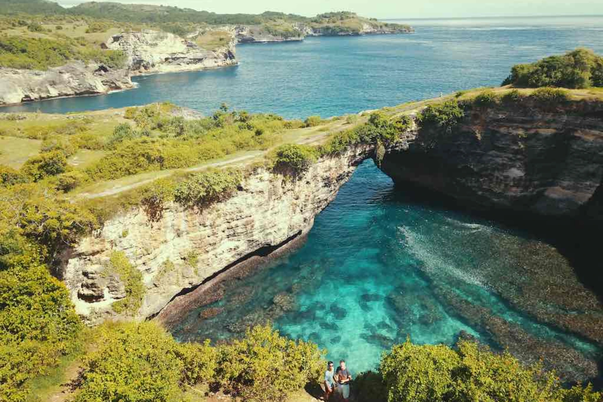Couple looking at blue water and rock arch at Broken Beach Nusa Penida
