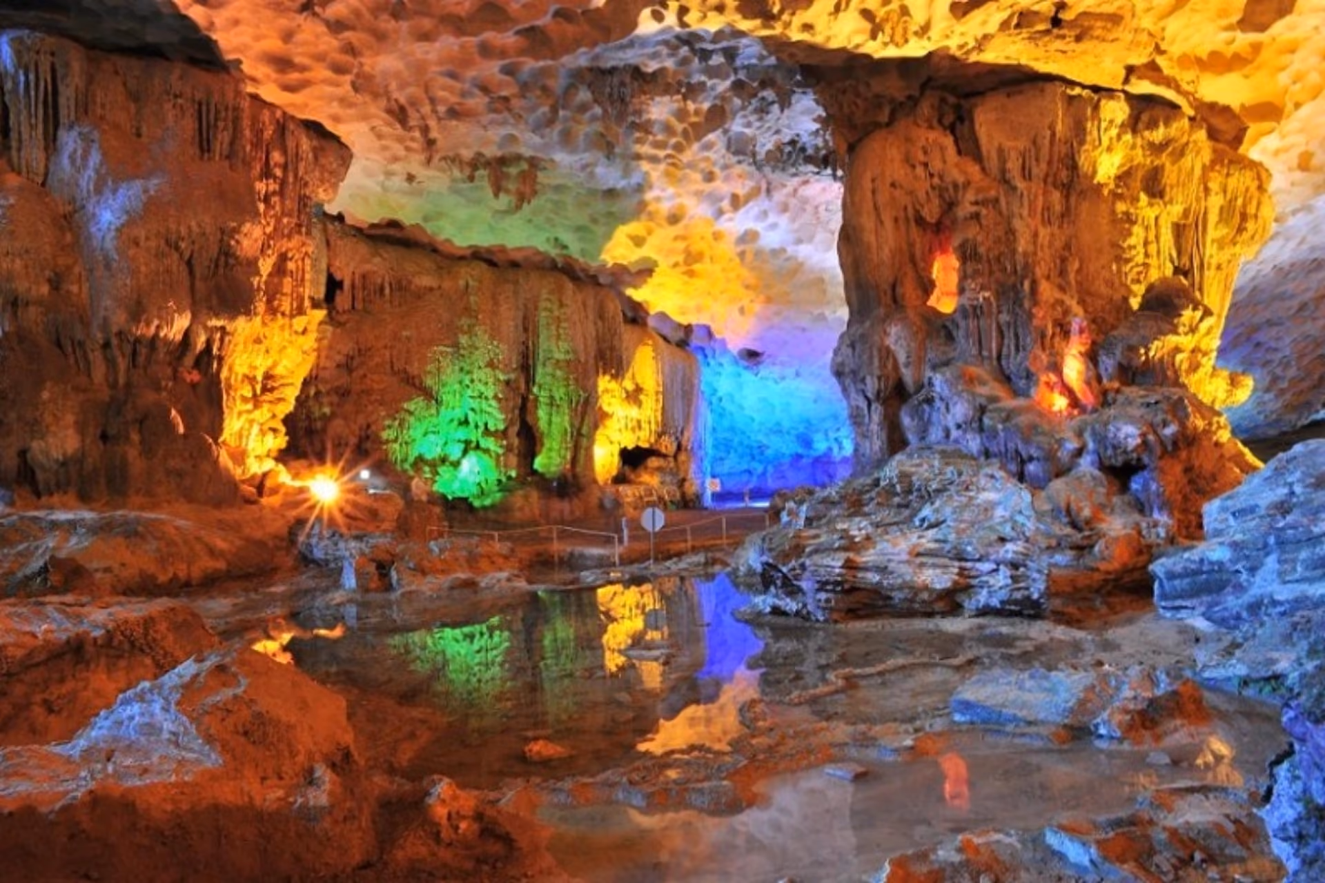 Colorful lit cave with water pool and stalactites