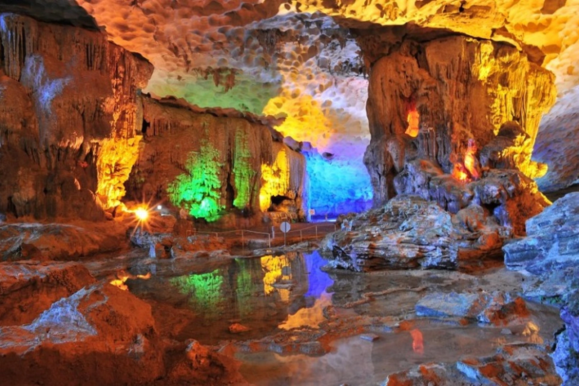 Colorful lit cave with water pool and stalactites