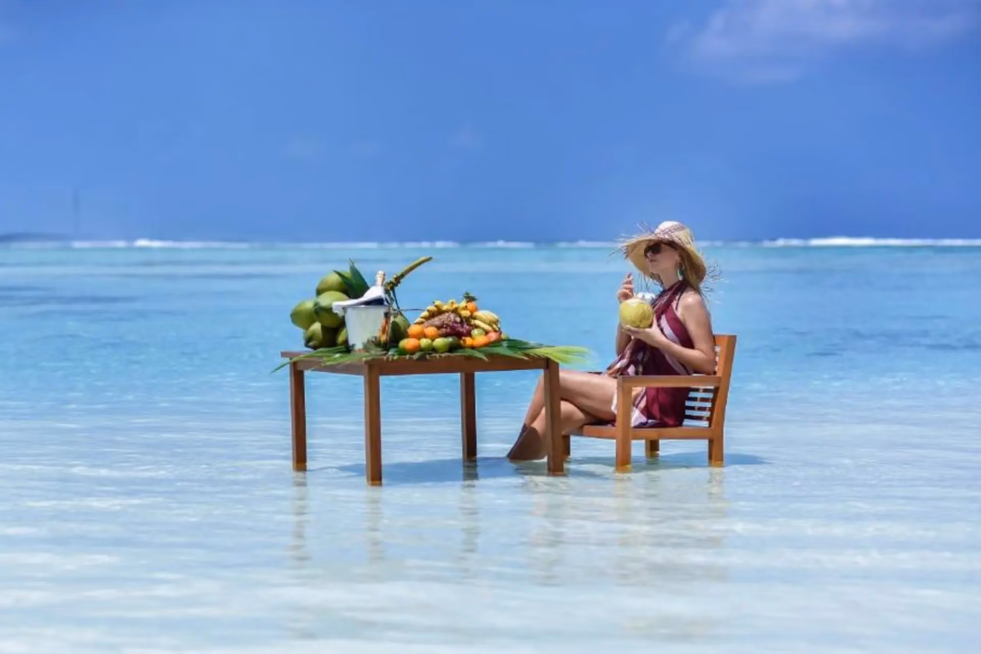 Woman sitting in shallow water at Adaaran Select with fruit table