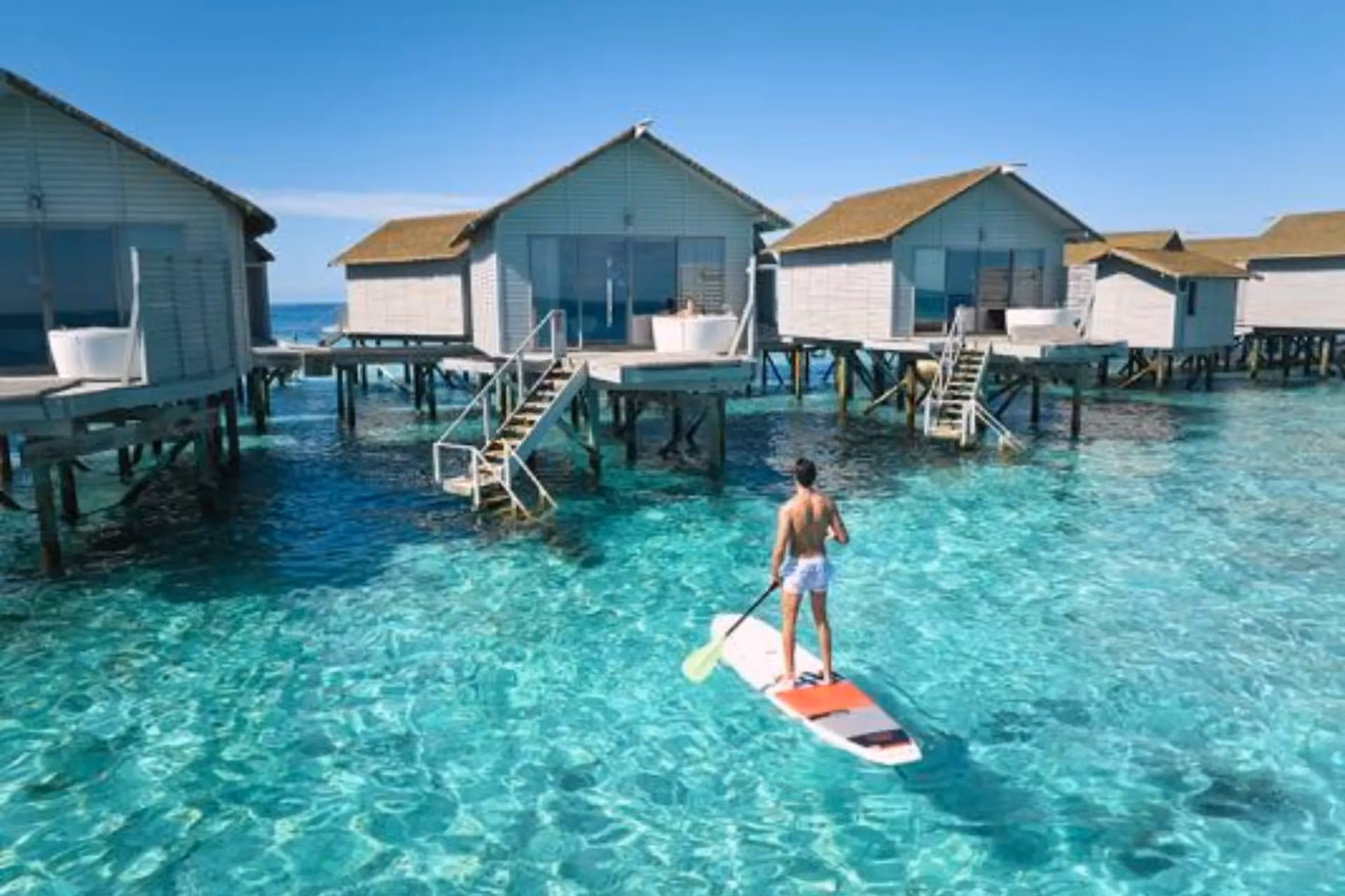 Man paddleboarding near wooden beach huts at Centara Ras