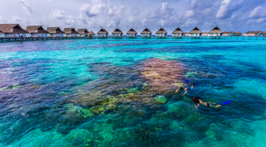 Snorkelers in clear blue water near overwater huts at Cirm