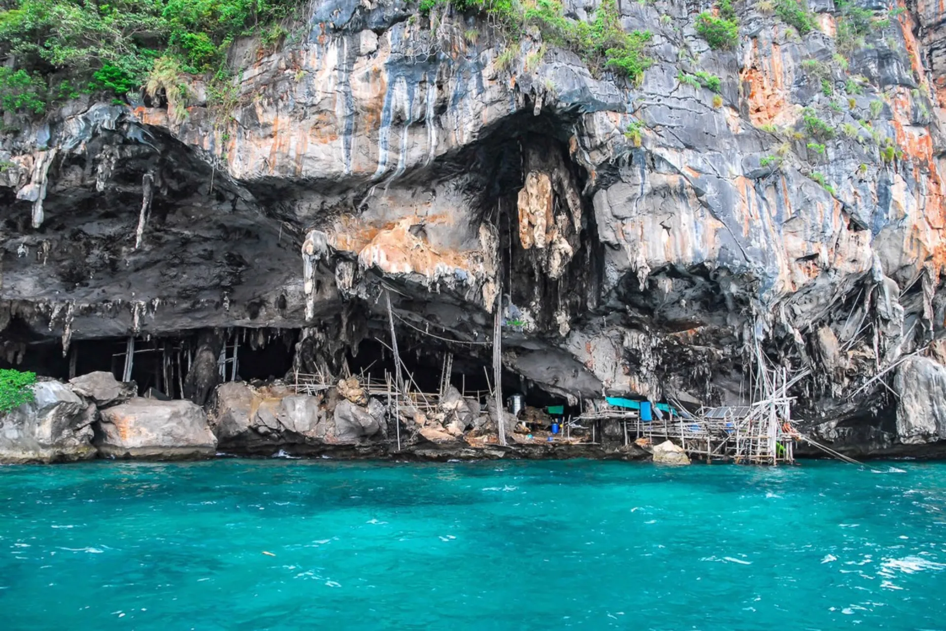 Large cave opening in tall rocky cliff by blue-green water