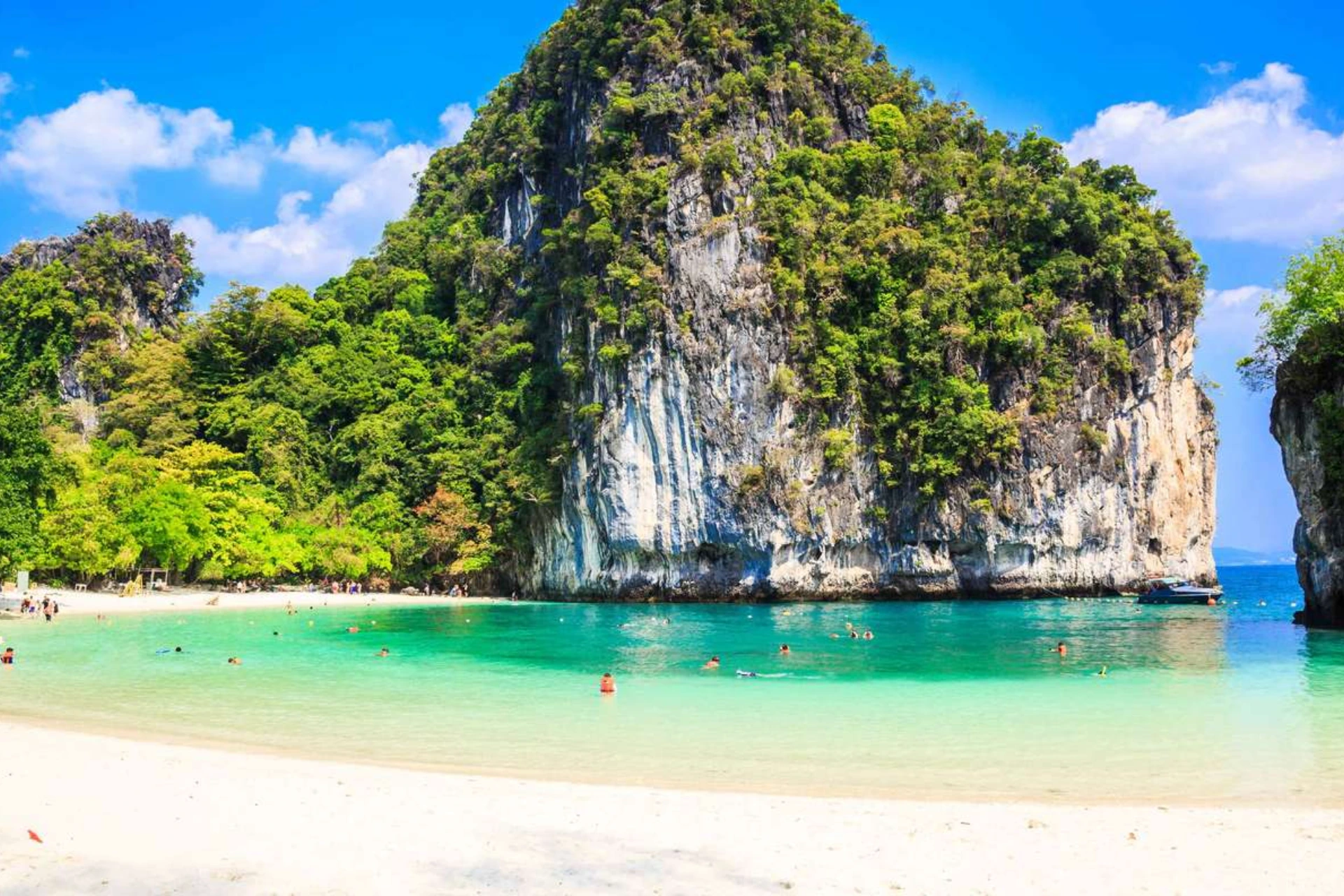 Tall rocky cliff with beach and green water at Hong Island