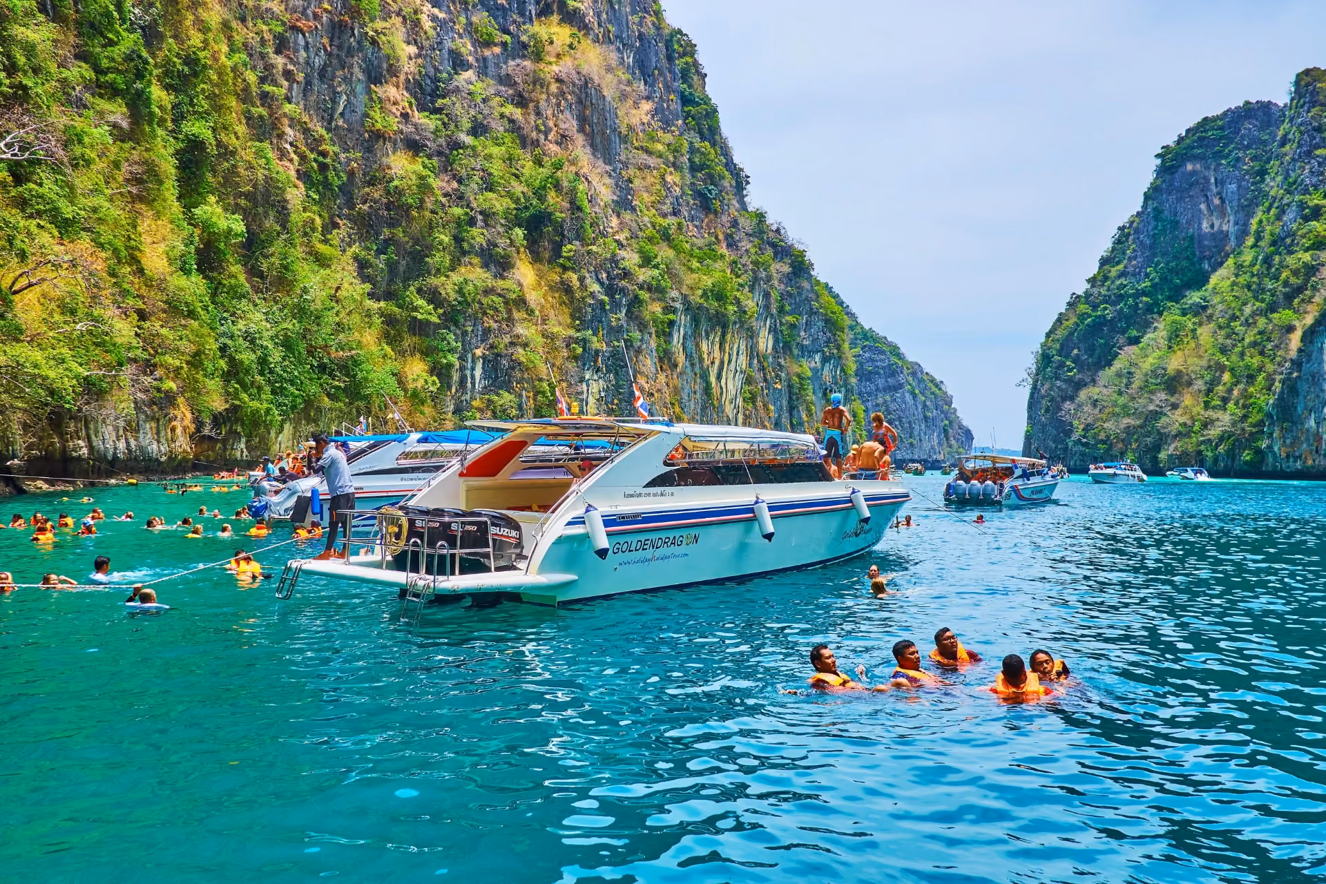 Tourists swimming near boats in Krabi's green water and cliffs